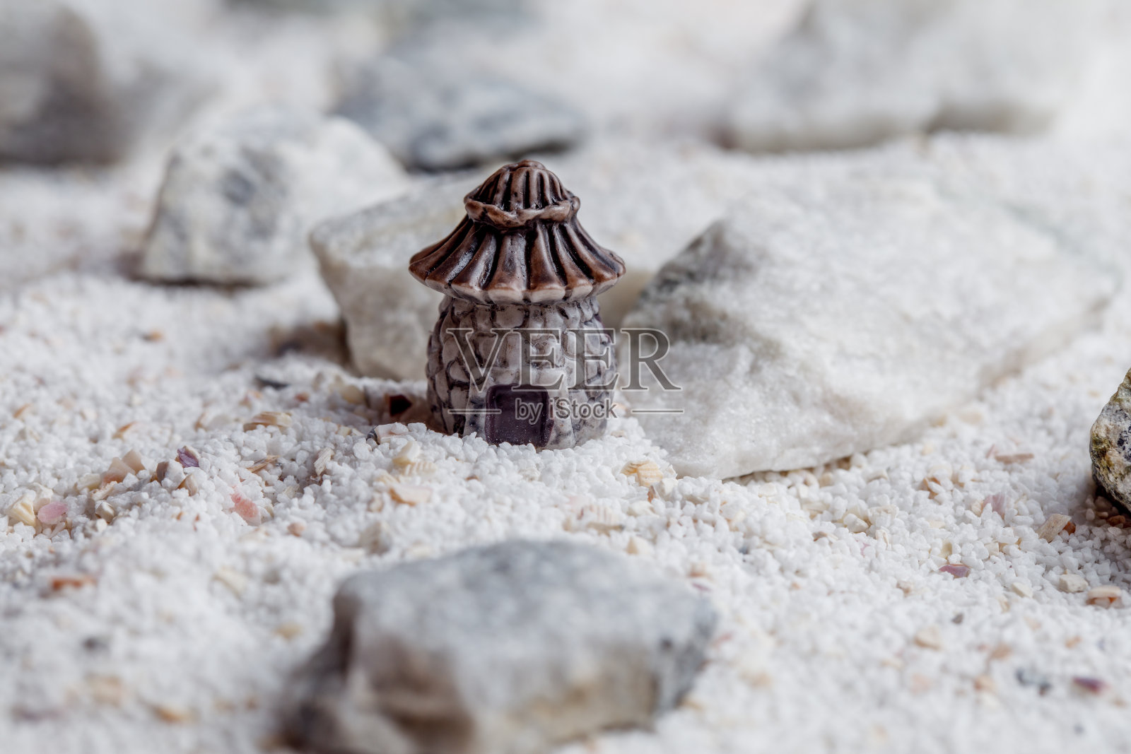 一座微型的房子，白色的沙滩上有石头和贝壳。照片摄影图片