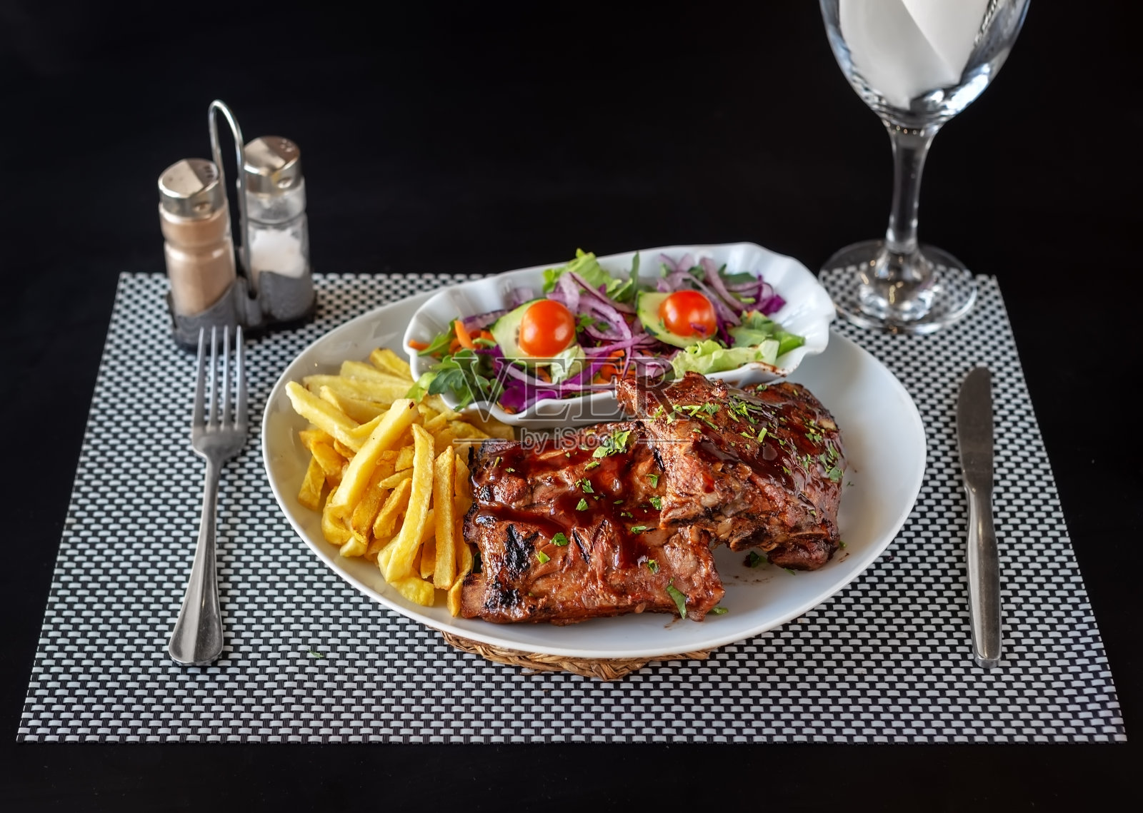 烤肋排配薯条和健康沙拉。刀叉和一杯水，摆好准备吃饭。照片摄影图片