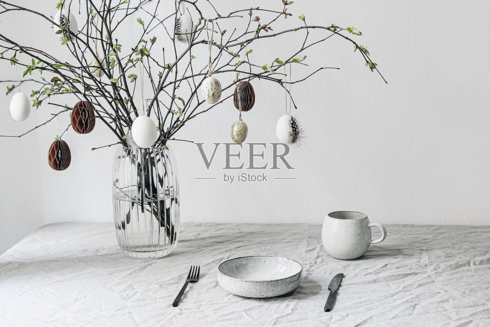 复活节餐桌布置。用纸装饰的花瓶里的新鲜树枝。挂着鹌鹑蛋。春天的室内装饰。斯堪的纳维亚设计最小。一杯咖啡。照片摄影图片