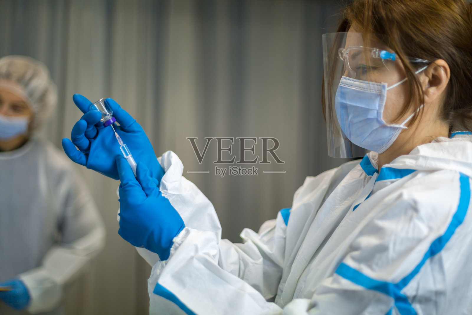 护士穿着防护服，手持注射器，注射COVID - 19疫苗照片摄影图片