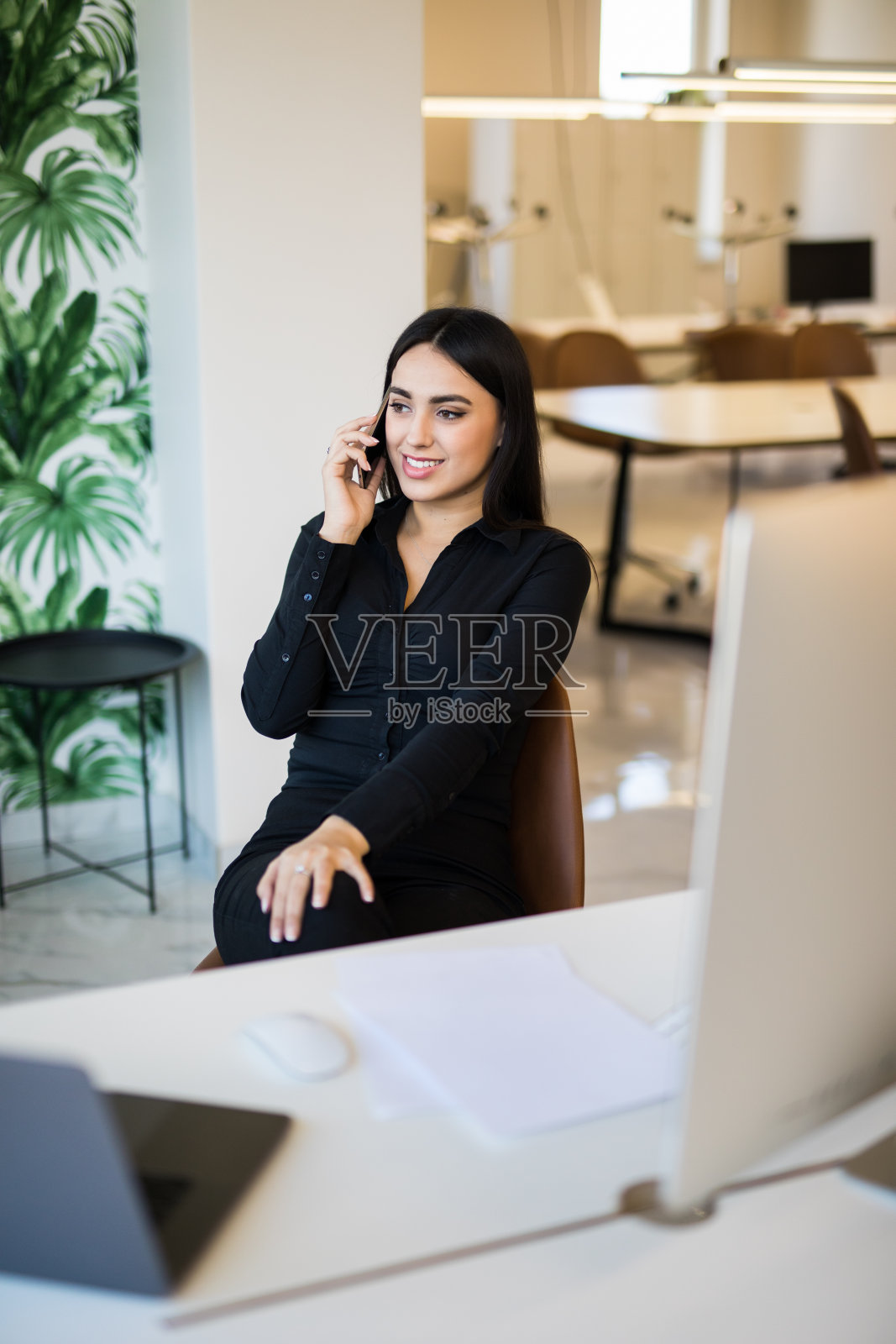 在办公室边打电话边用笔记本电脑工作的商业女性照片摄影图片