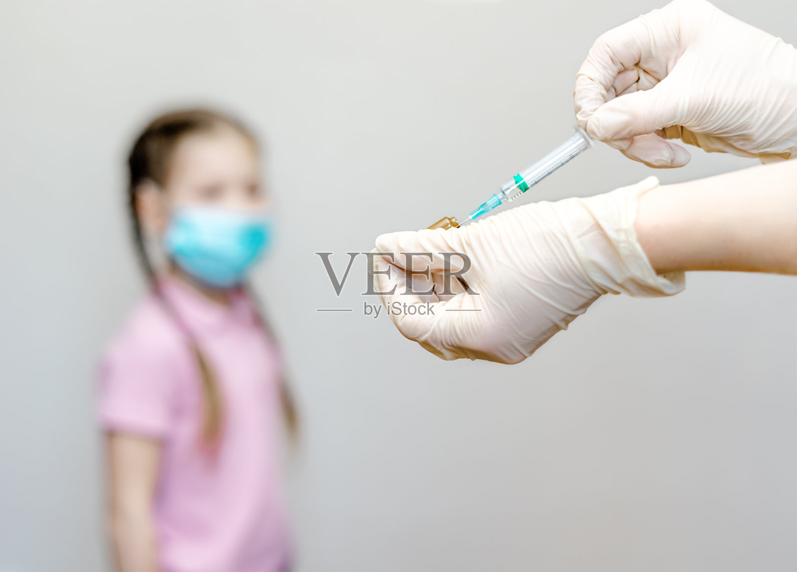 医生(护士)戴医用手套，手持注射器，从安瓿中抽取液体疫苗(药物)。像少女的注入。儿童保健和疫苗概念。背景中的孩子照片摄影图片