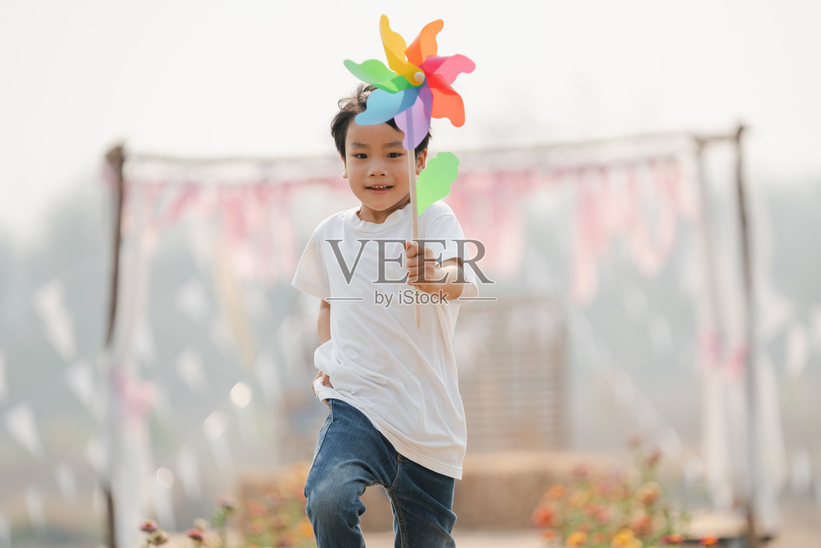 男孩拿着玩具风车快乐地在公园里跑步照片摄影图片