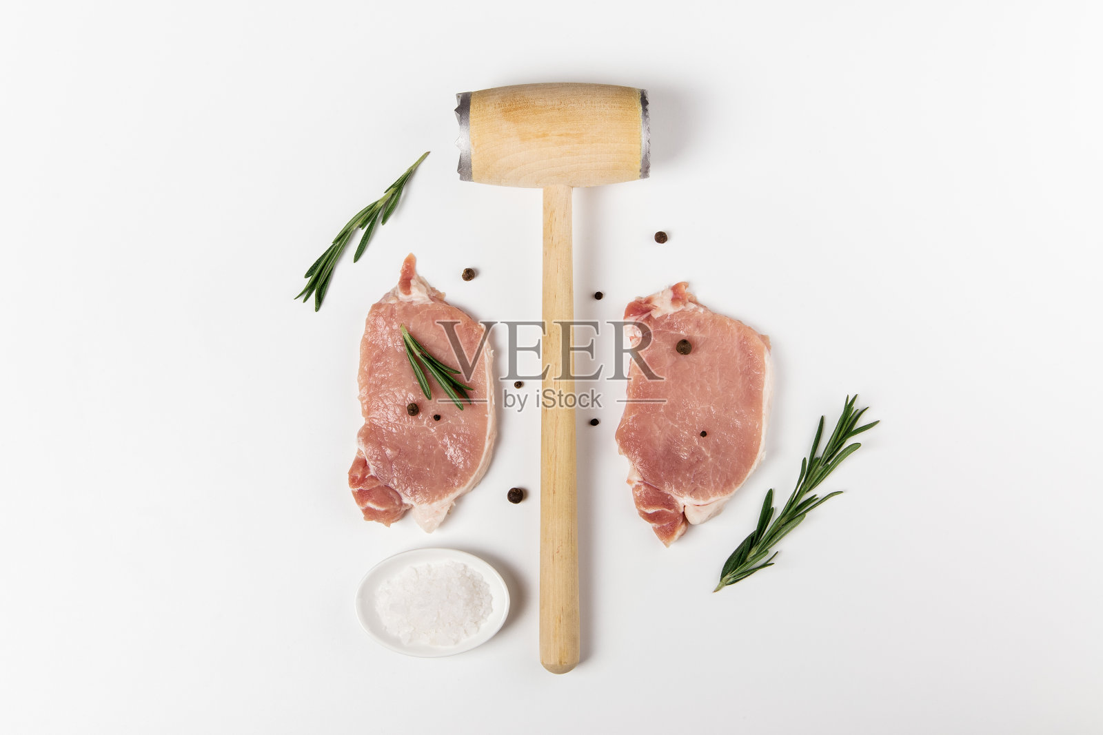 用迷迭香、盐和胡椒粉拌生猪肉。俯视图上的白色背景和厨房锤子照片摄影图片