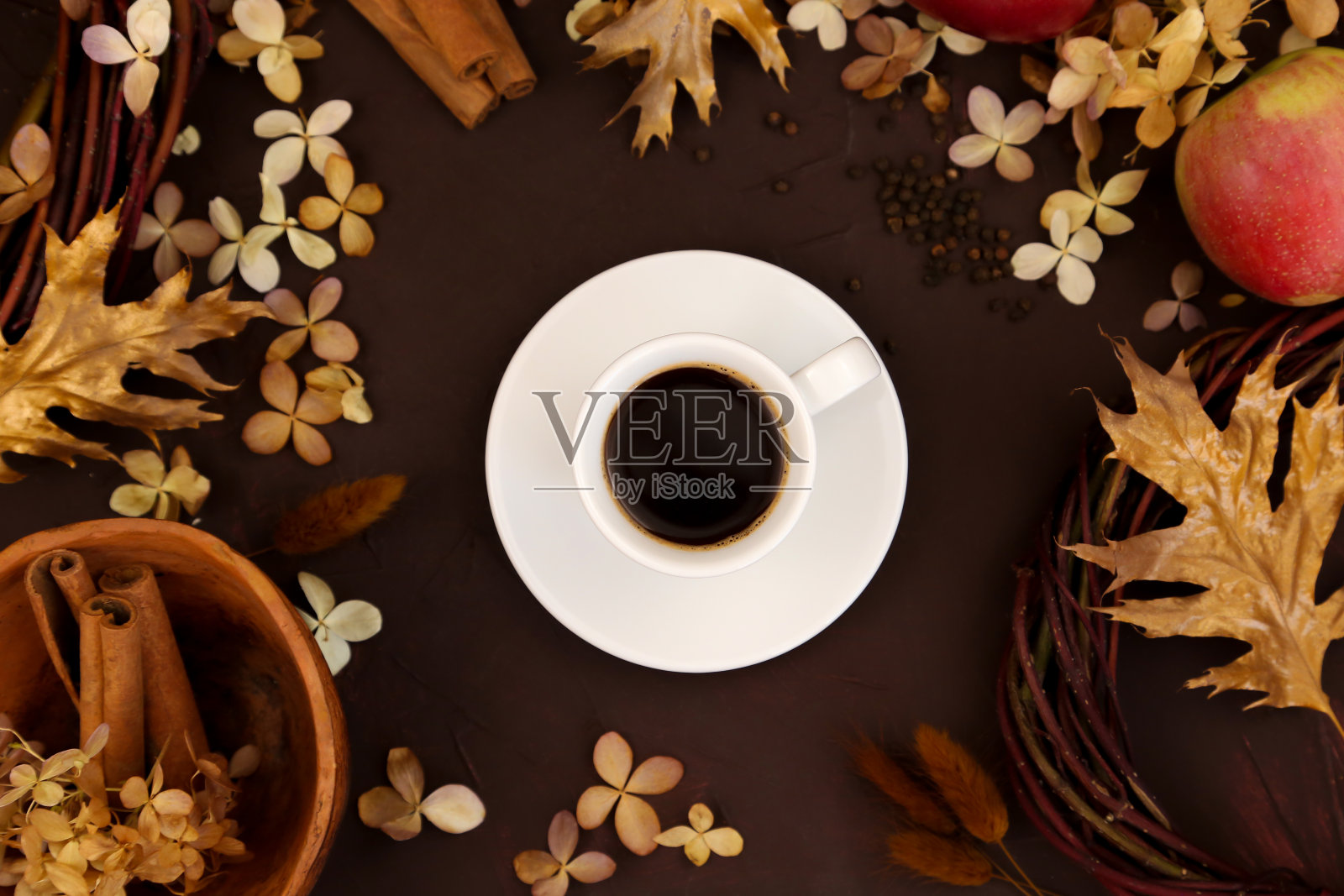 白色咖啡杯，秋叶，肉桂，苹果和干绣球在深棕色的背景，俯视图。秋天的概念。照片摄影图片