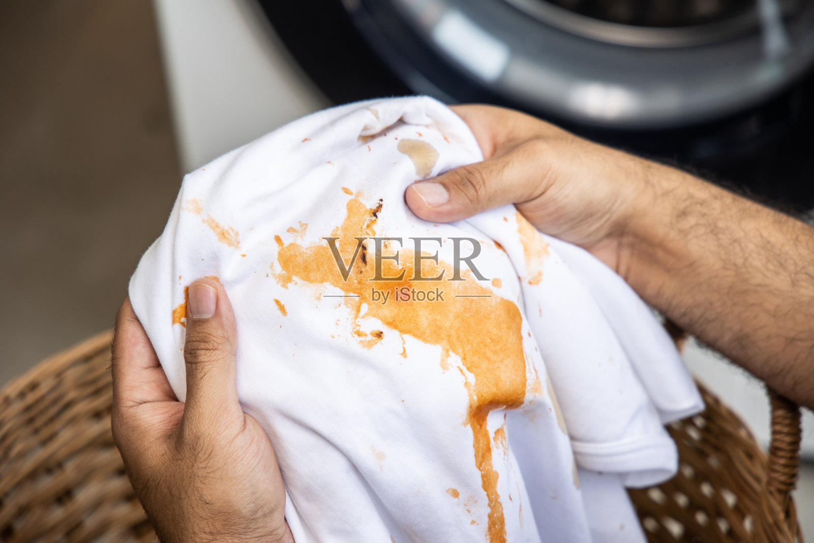 白色棉质衬衫很多污渍，污渍，咖啡污渍，男人的手把衬衫举起来，让它看起来很脏，必须拿去洗衣机洗照片摄影图片