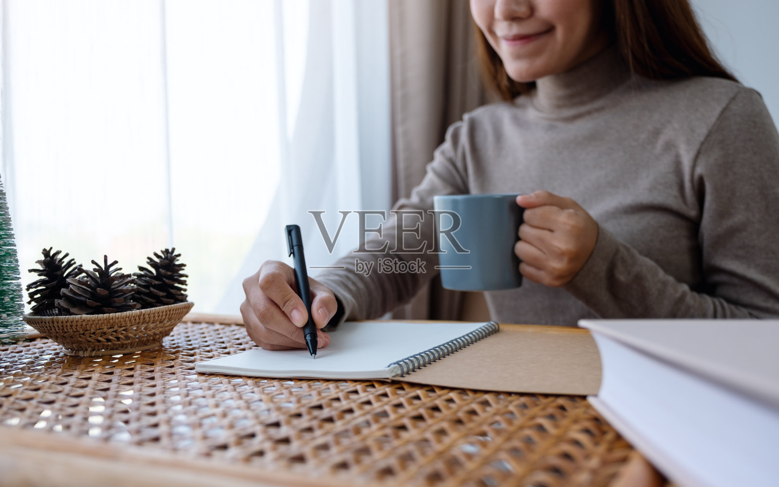 一个年轻的女人写在笔记本上，喝着咖啡在家里学习照片摄影图片