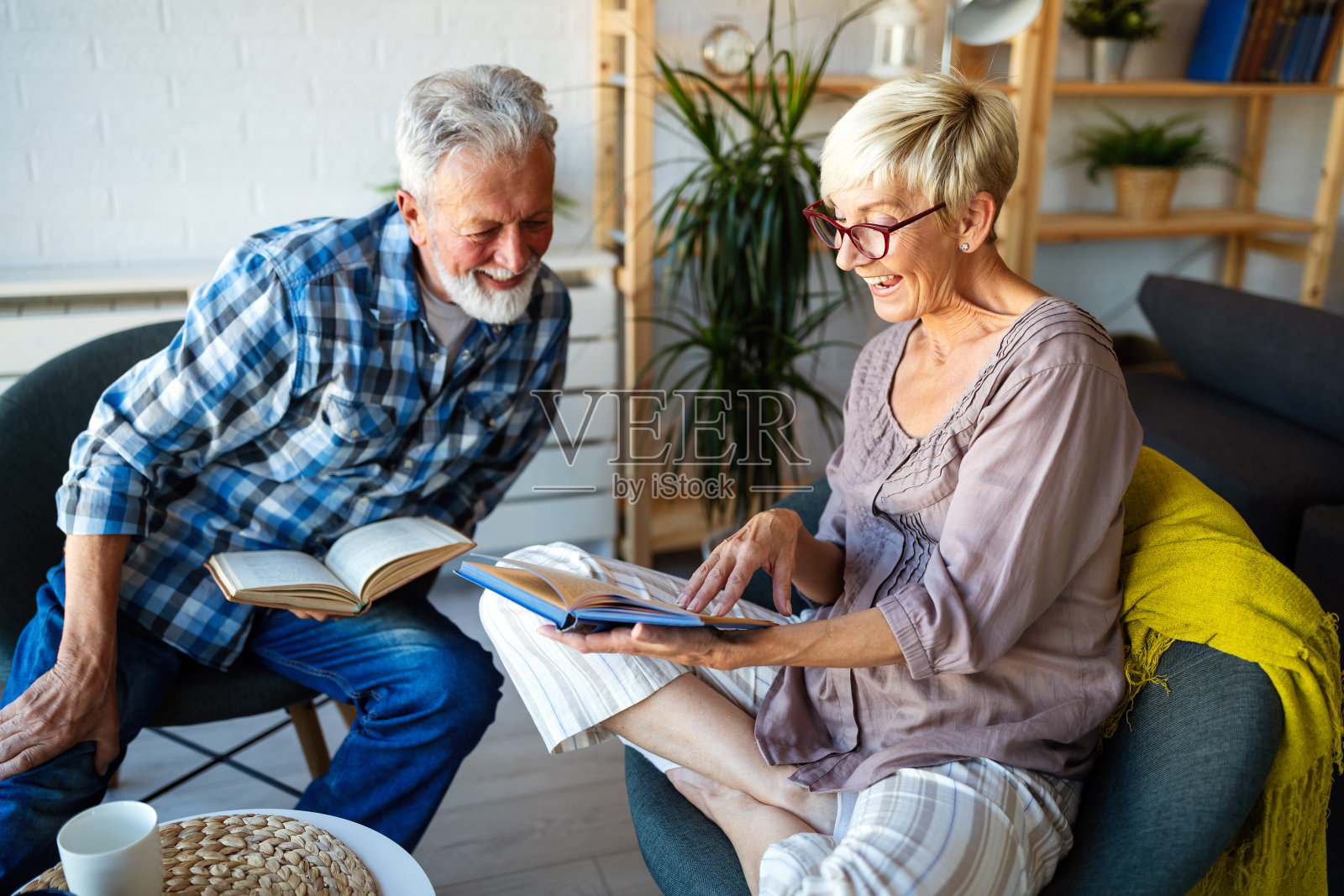 一对美丽的老夫妇正在家里微笑着看书照片摄影图片