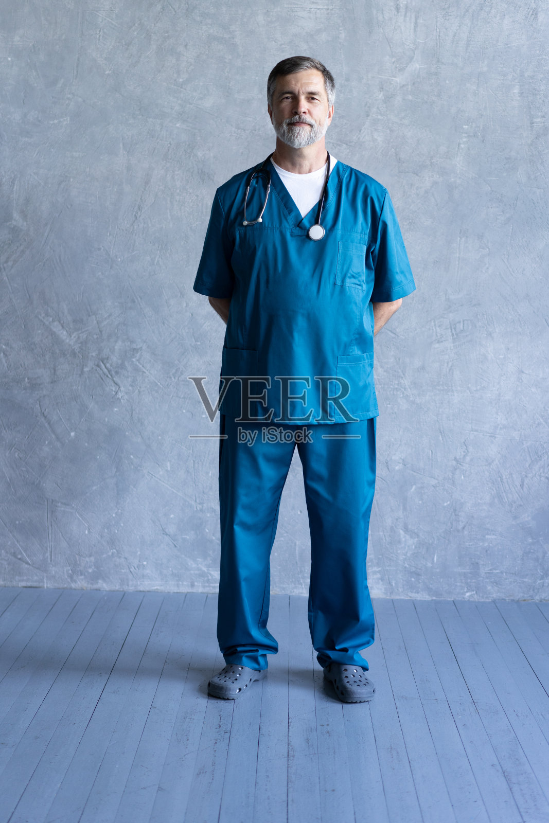 全长肖像的专业成熟的外科医生看着相机，而站在灰色背景。照片摄影图片