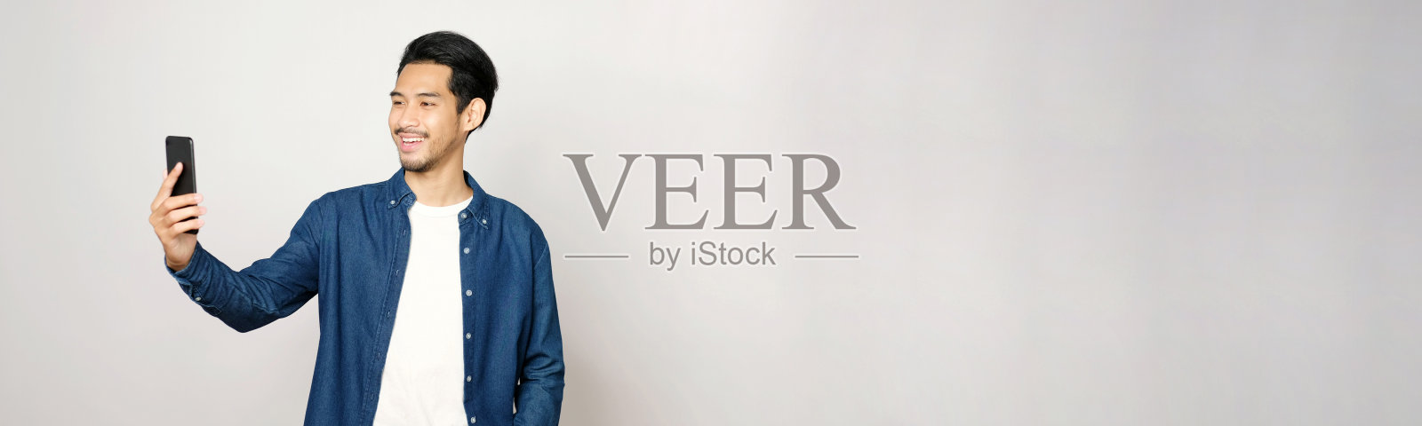 视频电话会议，快乐的亚洲人有一个视频聊天手机，而站在灰色背景与拷贝空间，亚洲男性在智能手机上谈论视频通话，人们使用在线电信，社交距离照片摄影图片