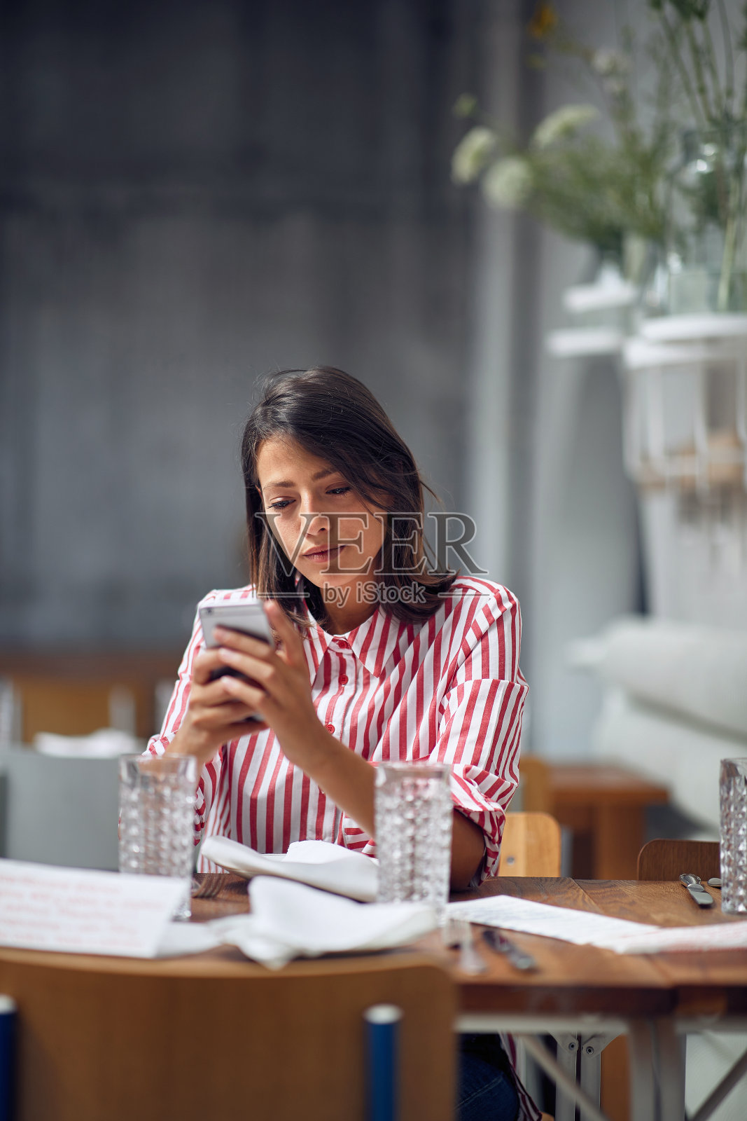 女孩坐在咖啡馆边吃边看手机。照片摄影图片