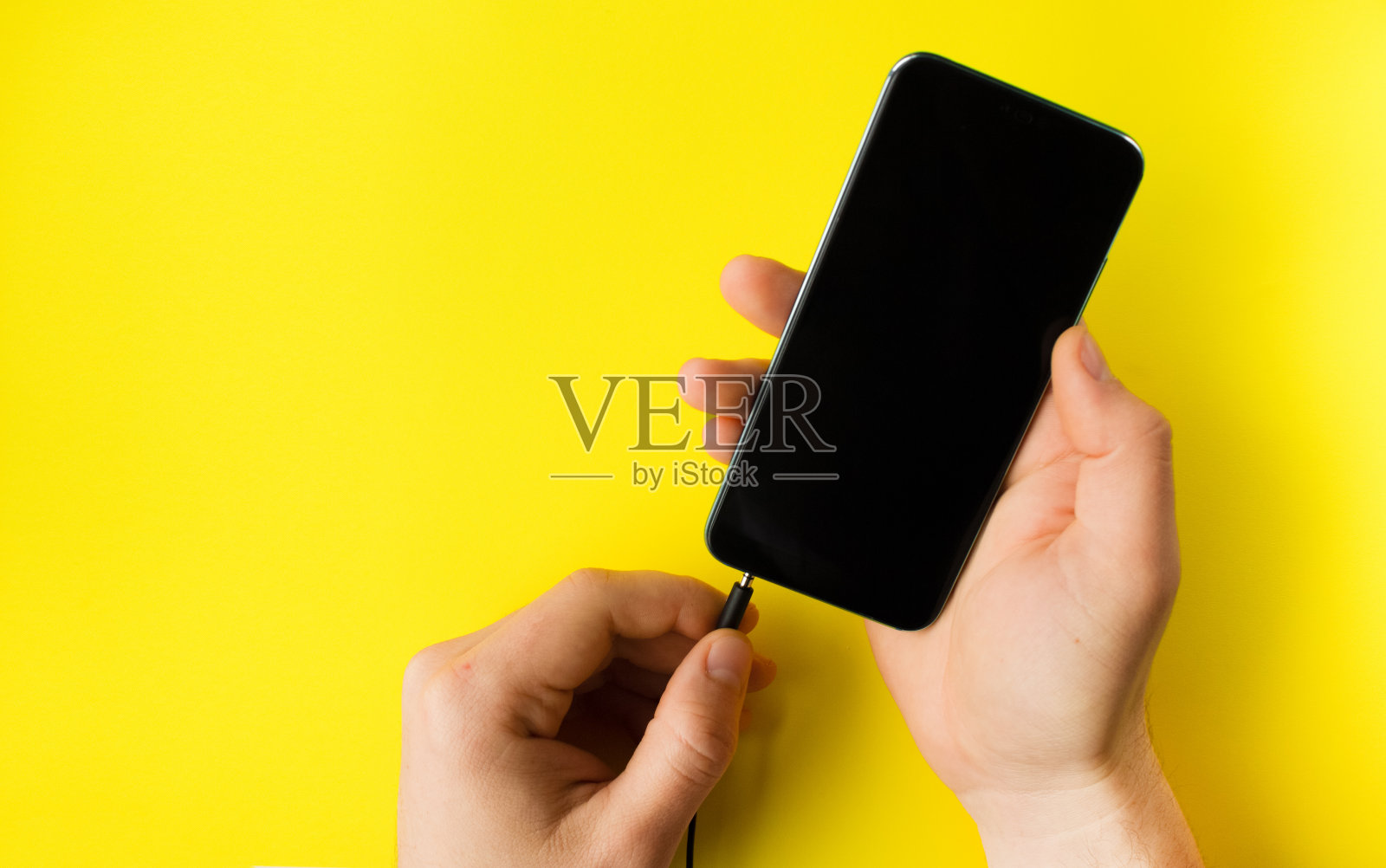 一只手拿着一部智能手机，另一只手在黄色背景上插入电缆照片摄影图片