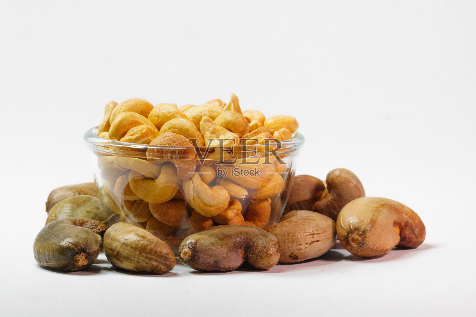 腰果在透明的玻璃杯和未剥皮腰果在白色的背景照片摄影图片