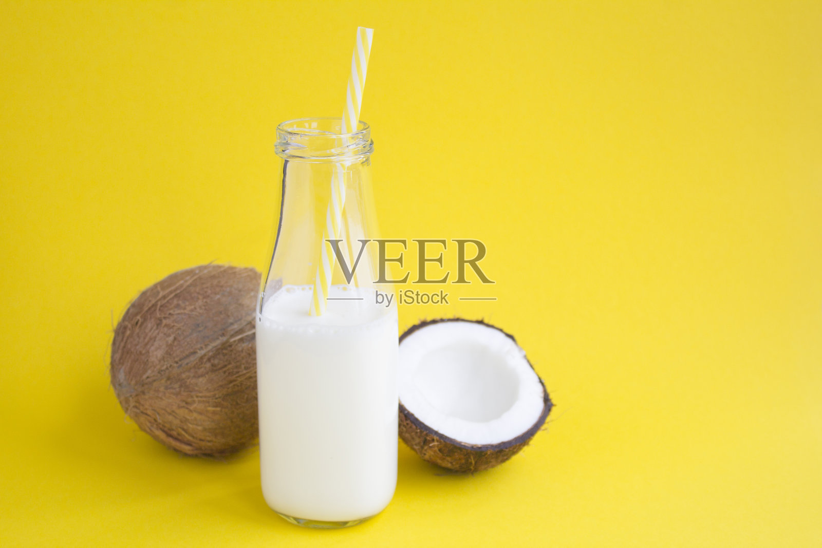 黄色背景上的玻璃瓶里的椰奶。副本的空间。照片摄影图片