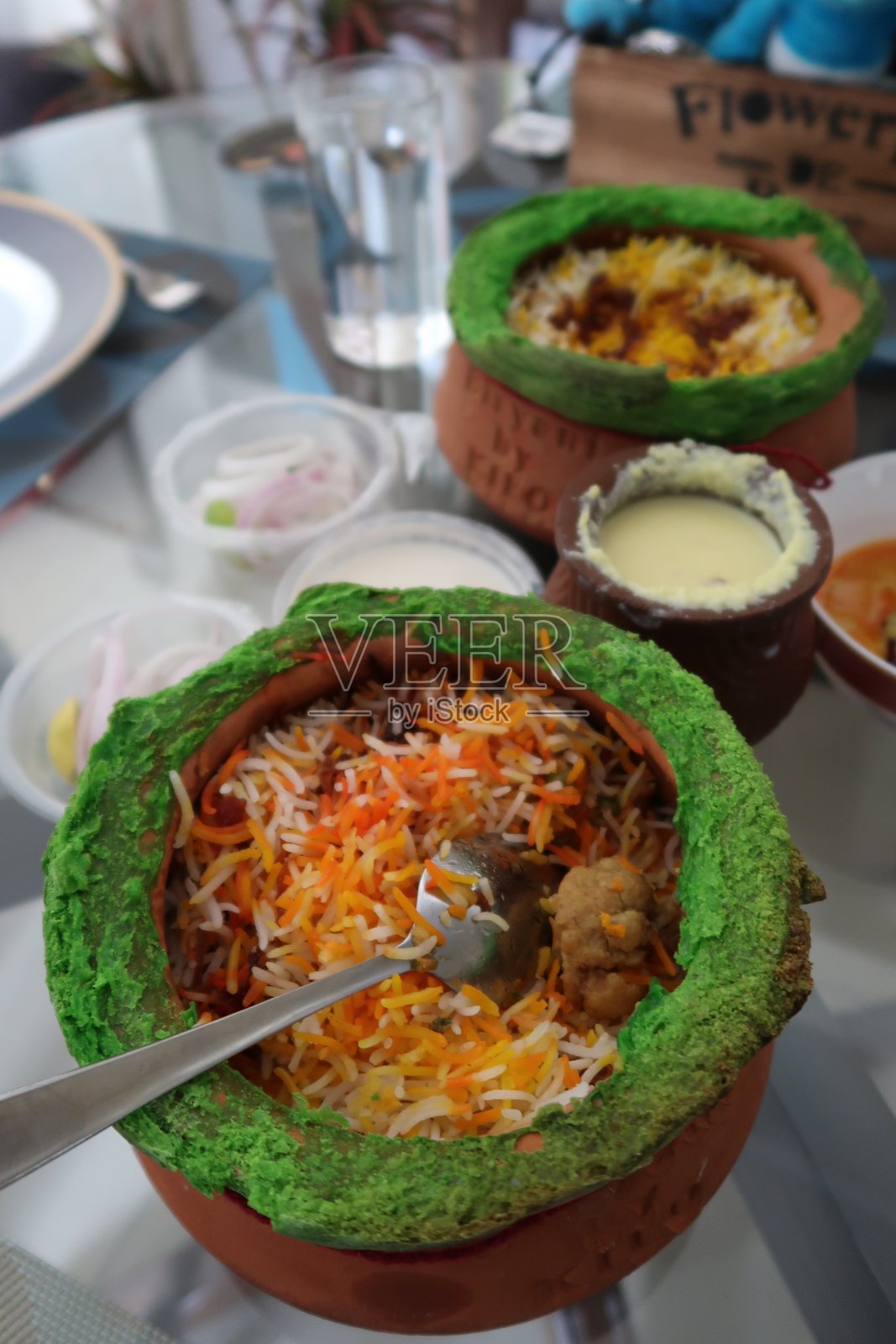 玻璃桌子上放着印度外卖，赤陶锅里盛着鸡肉饭，配上鸡肉调味汁和洋葱圈照片摄影图片