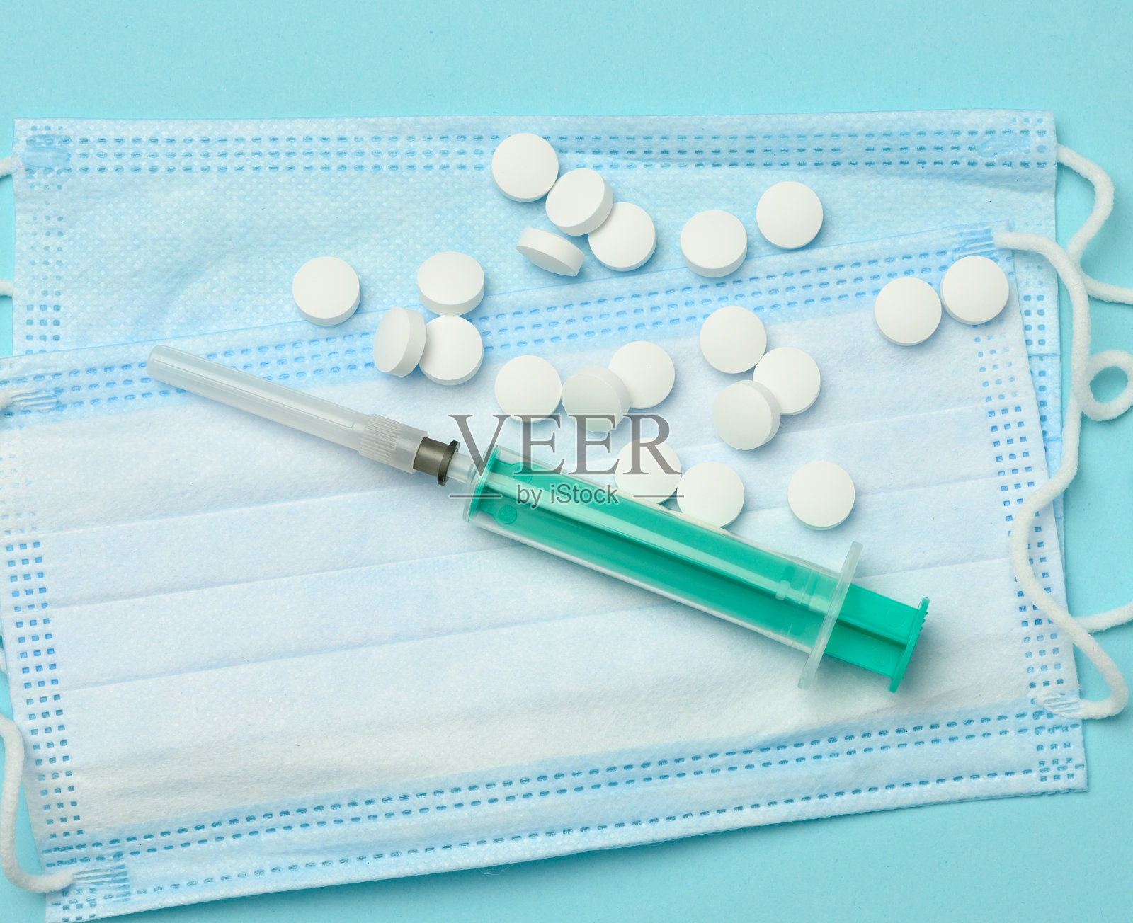 白色的圆药丸躺在一次性医用口罩上，蓝色的背景照片摄影图片