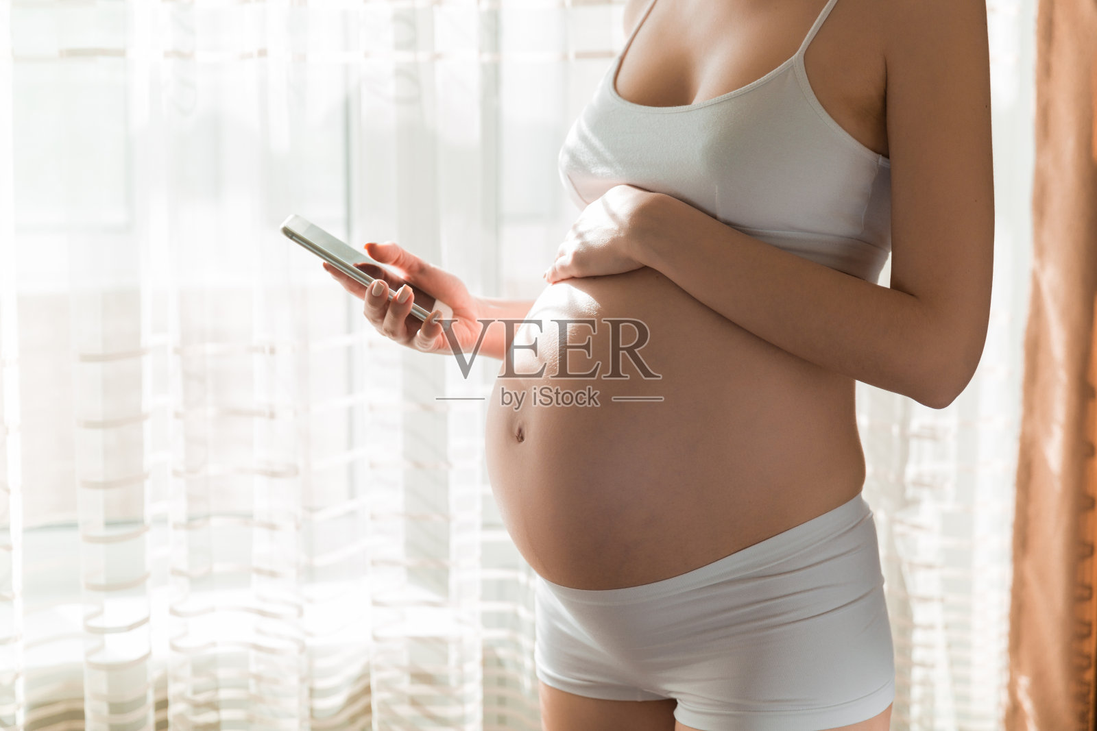 年轻漂亮的孕妇站在窗边在家发短信照片摄影图片