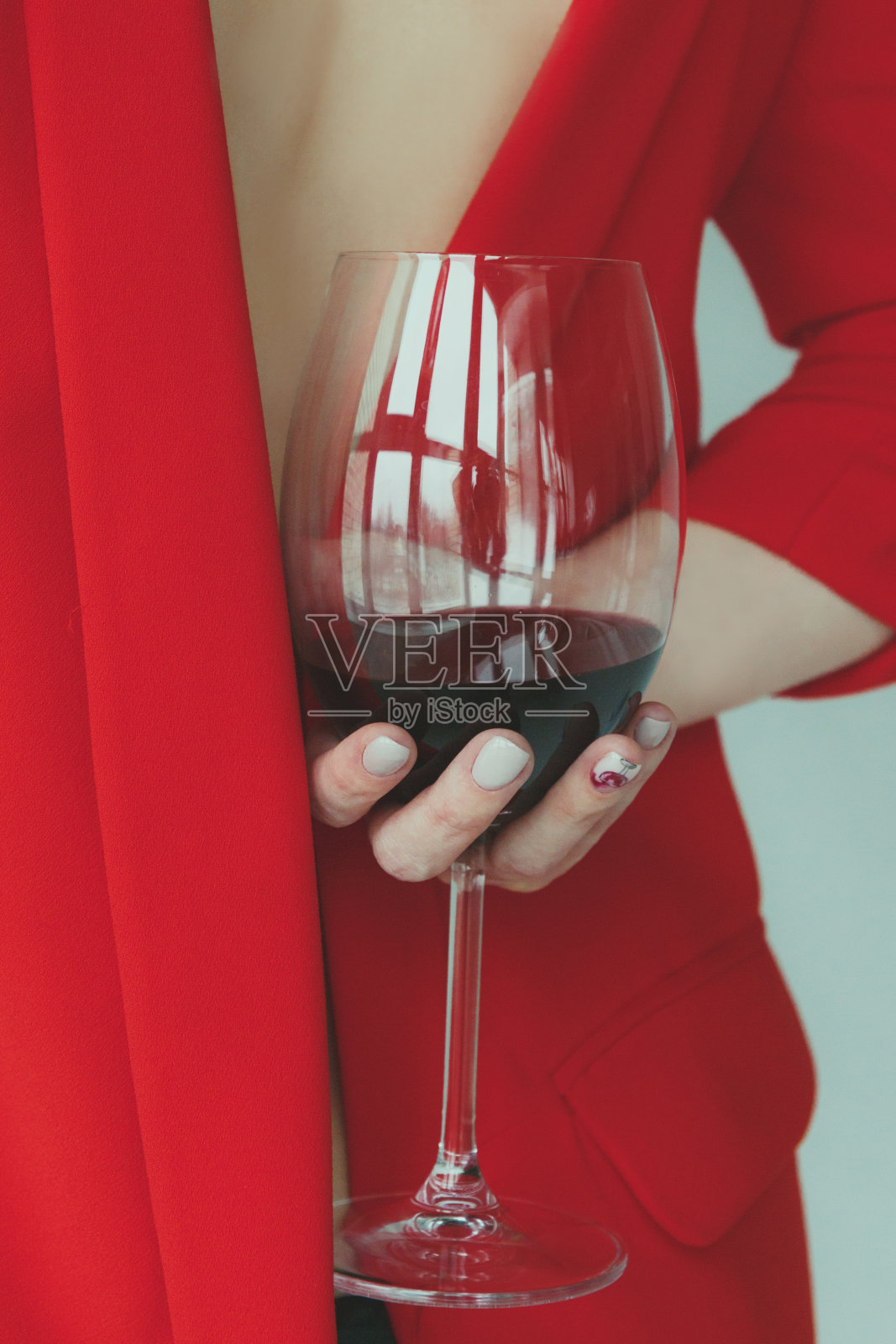 一名身穿红色夹克的年轻女子在背后举着一杯红酒照片摄影图片