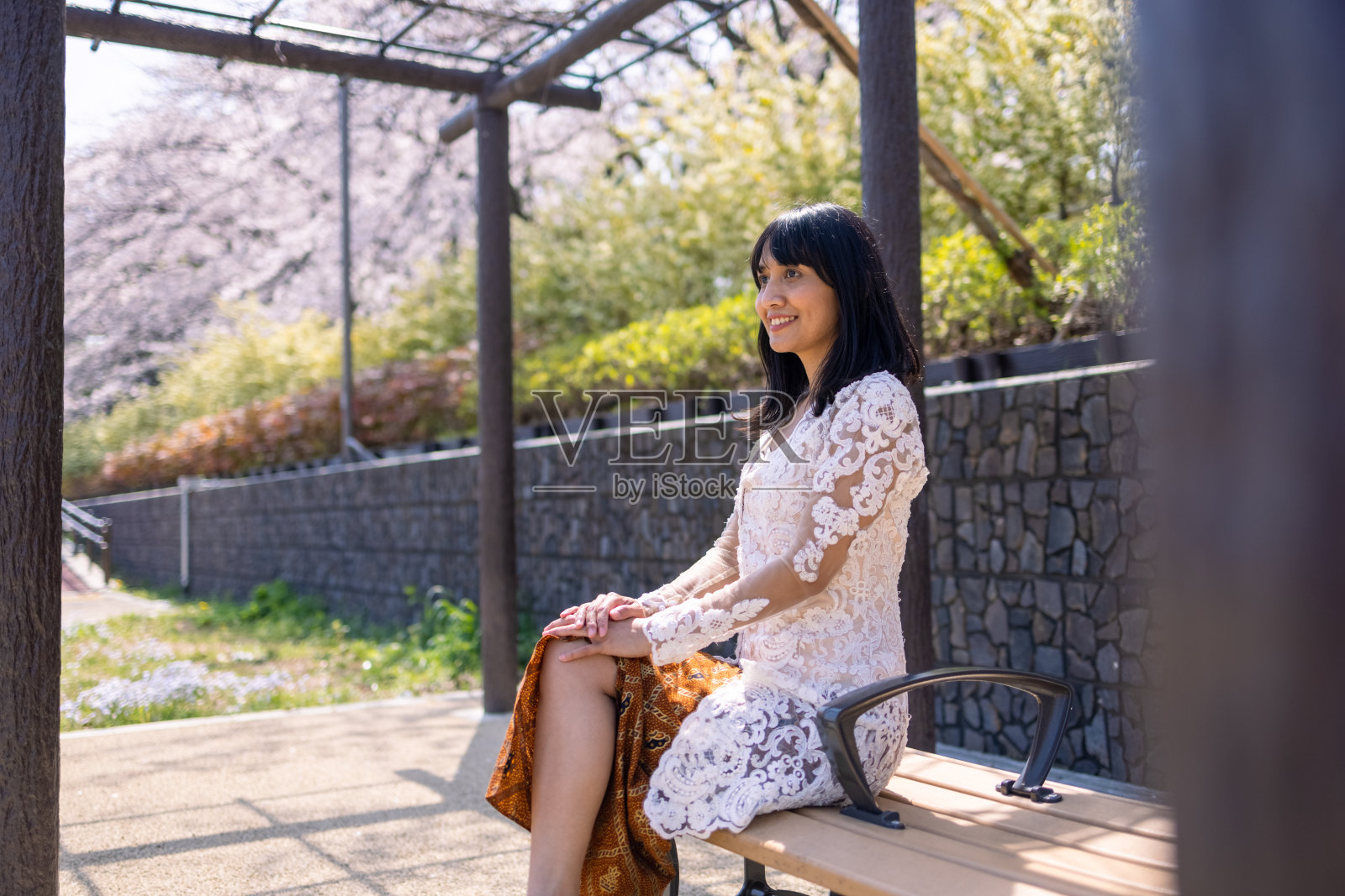 亚洲妇女在传统印度尼西亚服装坐在樱花下的长凳上照片摄影图片