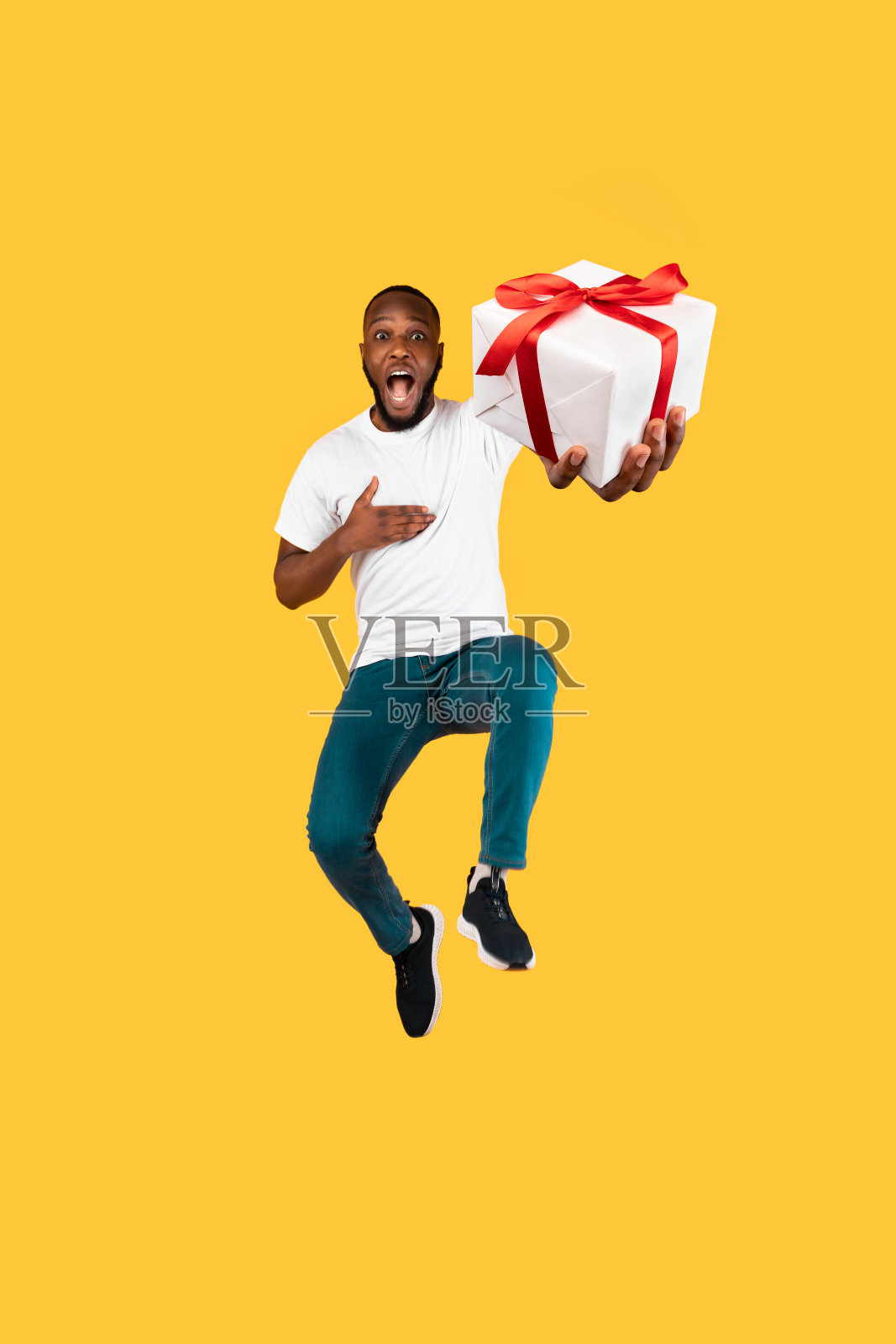 滑稽的黑人男子跳拿着礼盒在黄色的背景照片摄影图片