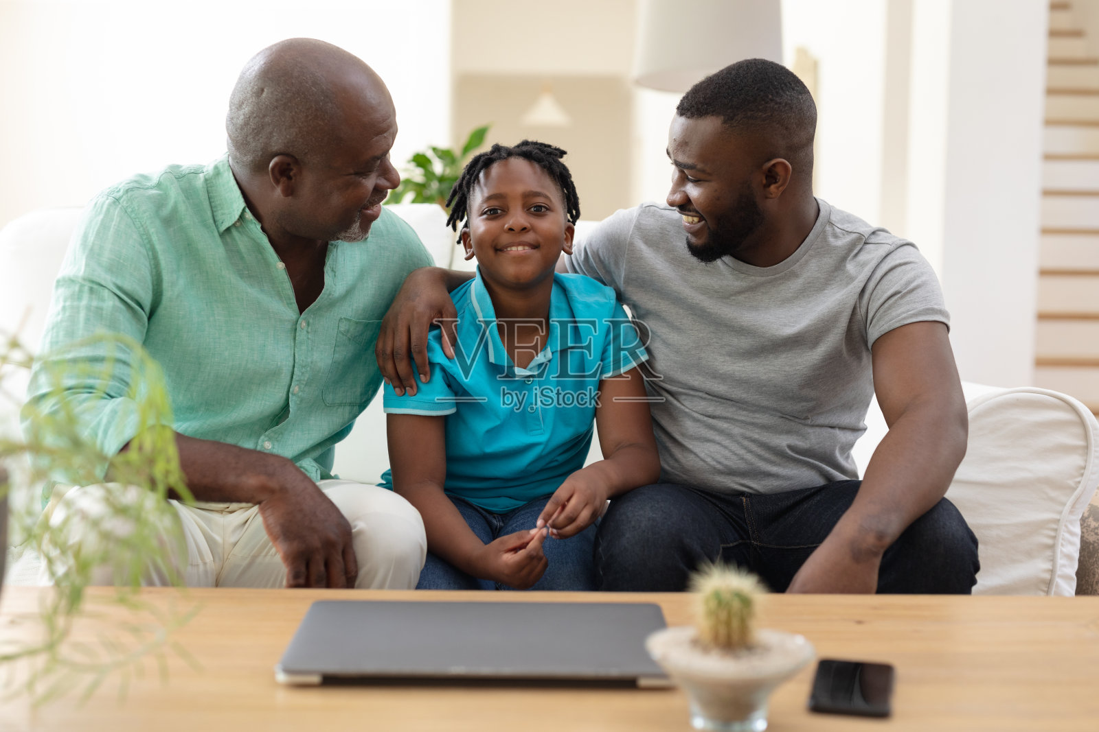 老非洲裔美国人祖父坐在沙发上和成年的儿子和孙子微笑照片摄影图片
