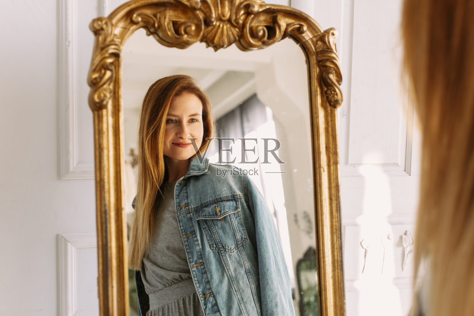 舒适的家庭氛围。穿着灰色裙子和牛仔裤的时髦红发女人坐在家里的椅子上照镜子。画像美丽的年轻女子幸福的微笑放松在客厅室内照片摄影图片