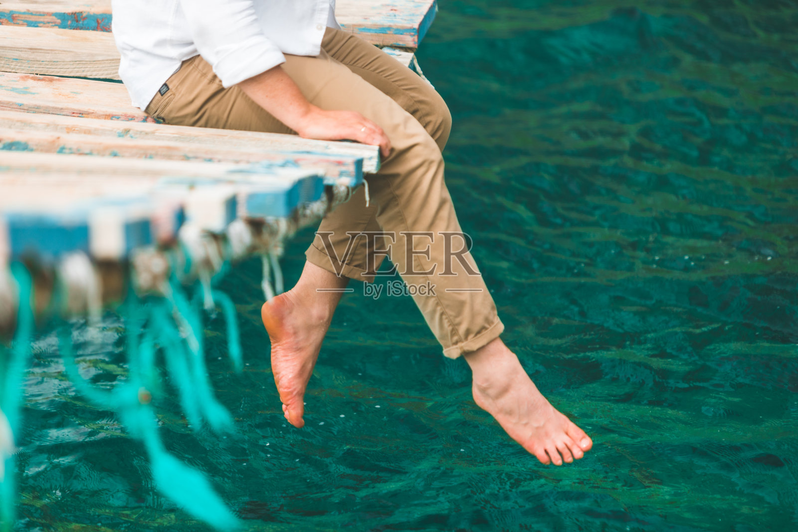 一名男子坐在吊桥上，把腿放在海水里照片摄影图片