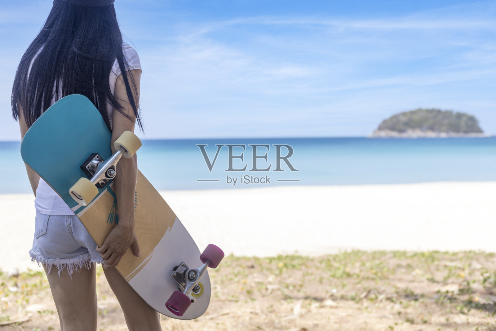 年轻女子持有冲浪滑板与海滩背景。女人站着冲浪，滑冰，放松和享受与复印空间的热带海滩照片摄影图片