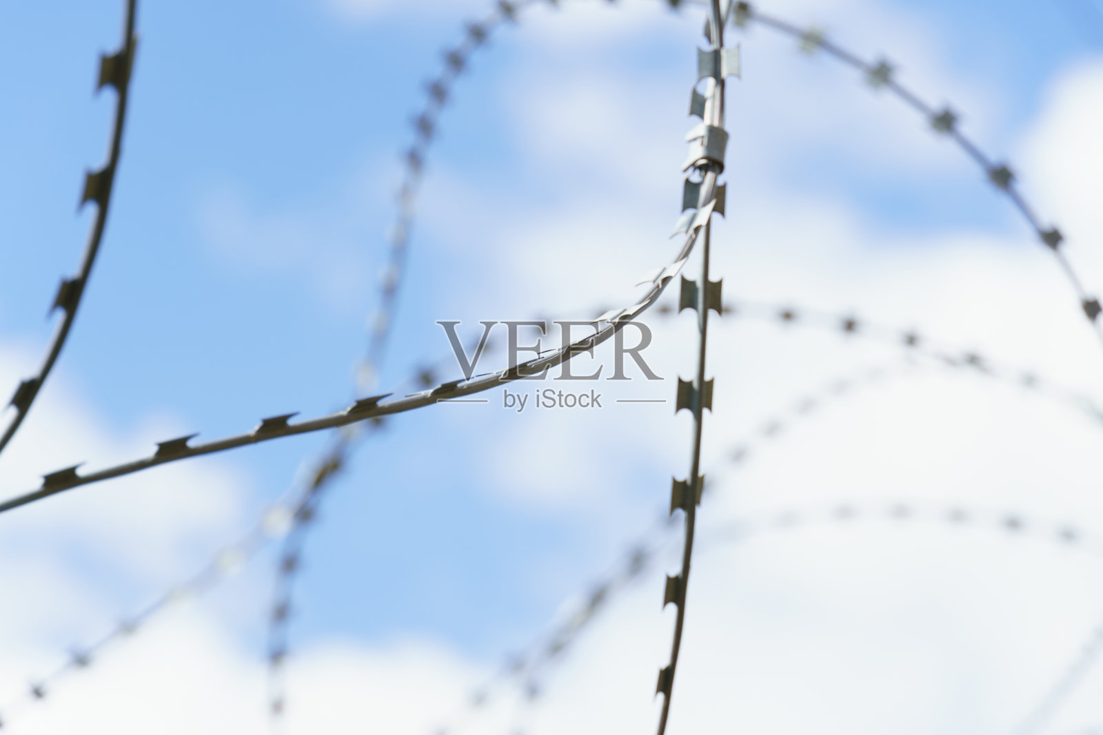 蓝天下保护着一家工厂的带刺铁丝网。照片摄影图片