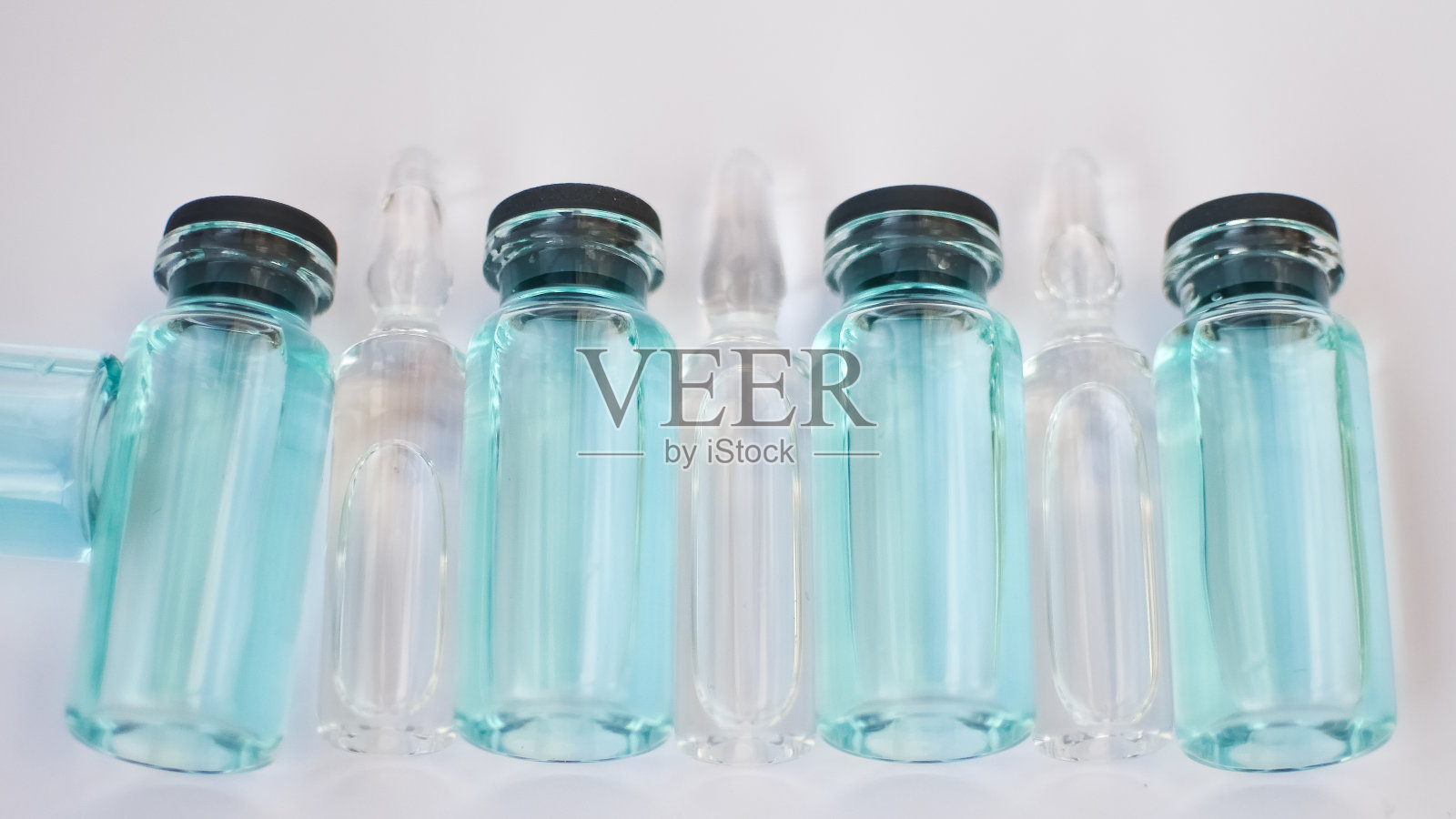 小瓶疫苗，俯视图的玻璃安瓿与透明和蓝色液体躺在白色背景，全球疫苗概念照片摄影图片