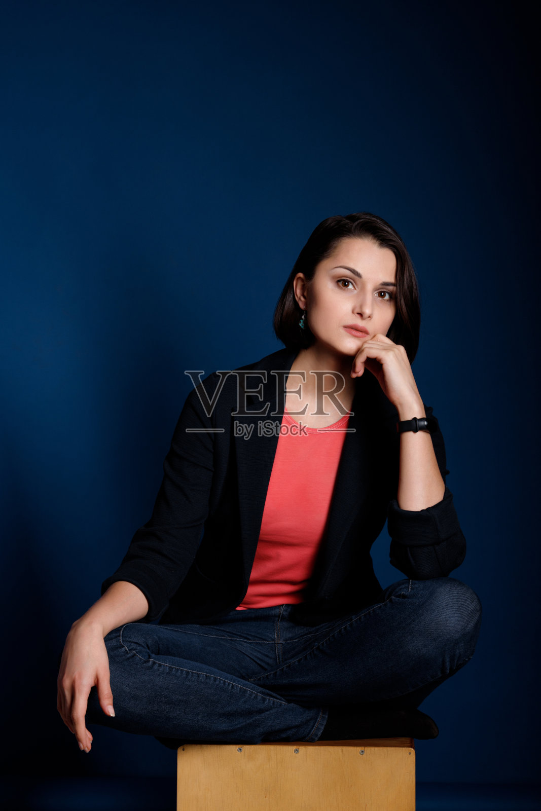 一个年轻的黑发女子的肖像，穿着珊瑚色背心，黑色运动夹克和蓝色牛仔裤在深蓝色的背景照片摄影图片