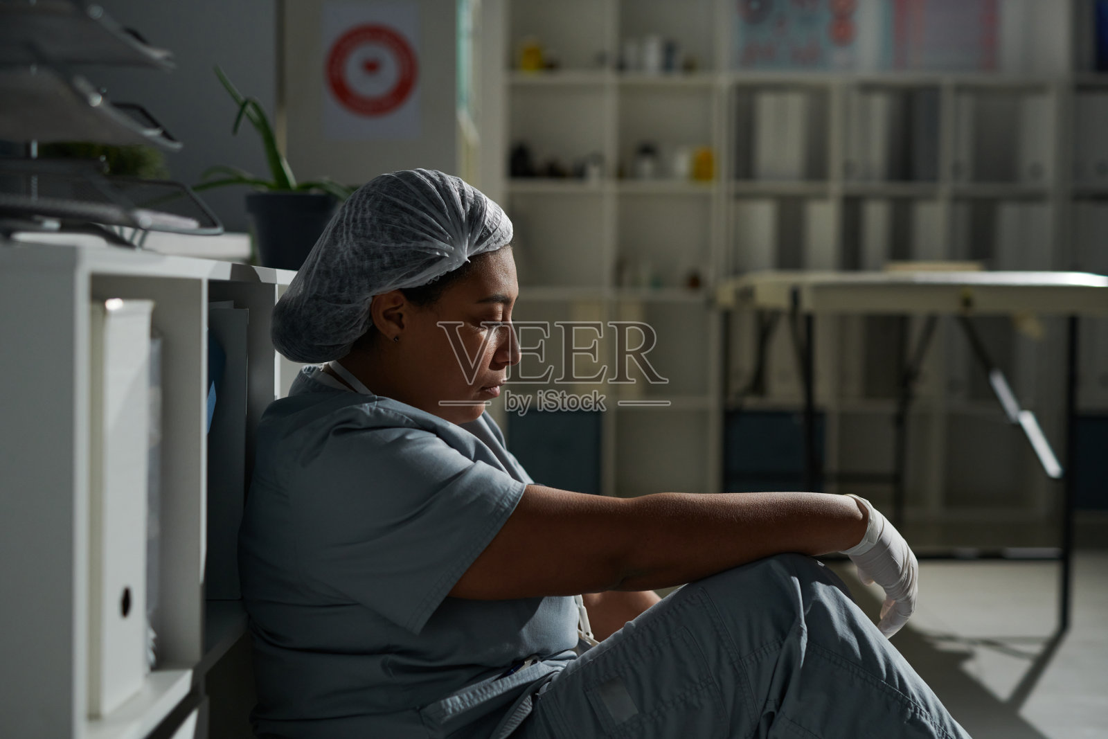 侧面的年轻疲倦的混血女临床医生在制服休息在地板上照片摄影图片