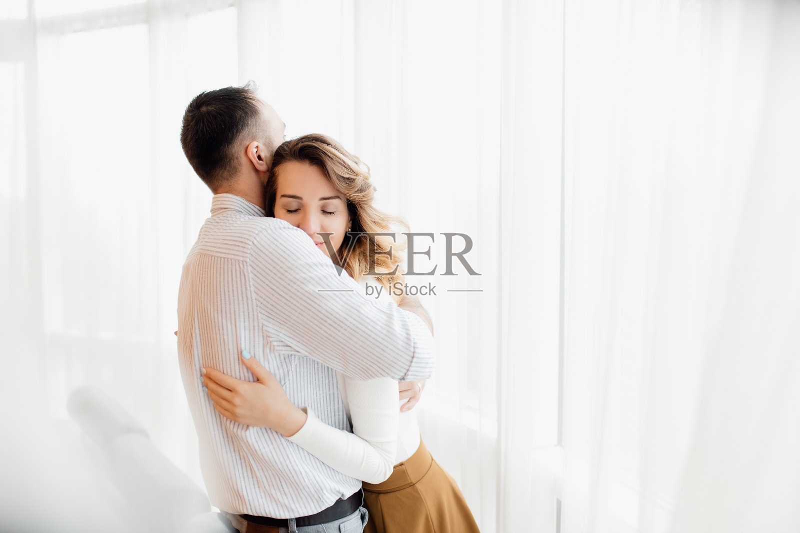 年轻的白人夫妇的肖像，男人抱着一个女人靠近窗口幸福的关系。照片摄影图片