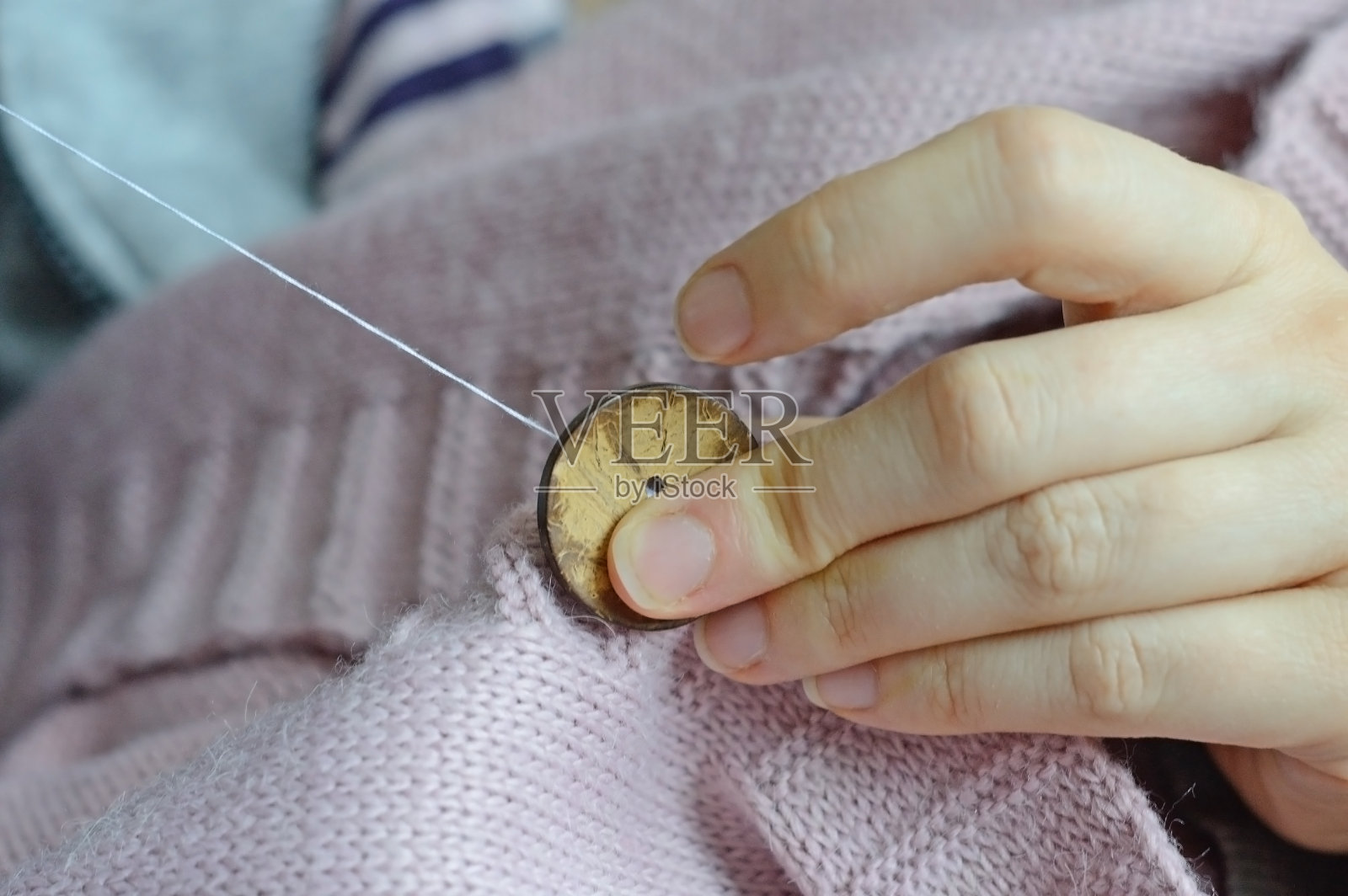 女工们用手把一颗木纽扣缝在夹克上。特写镜头。照片摄影图片