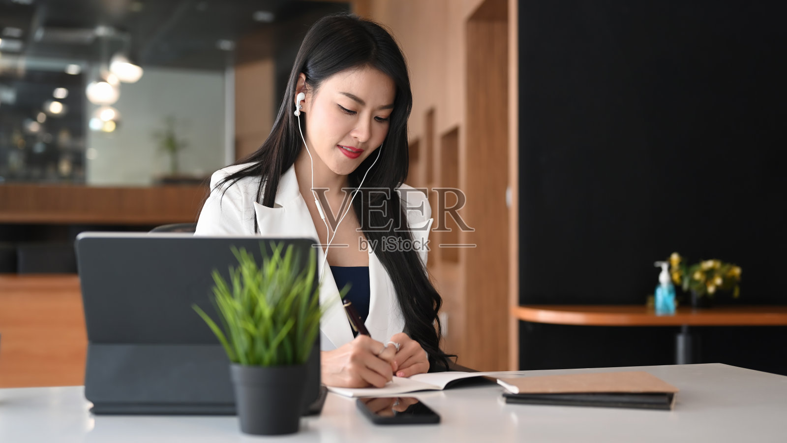 年轻的女商人一边用耳机听音乐一边在办公室工作。照片摄影图片