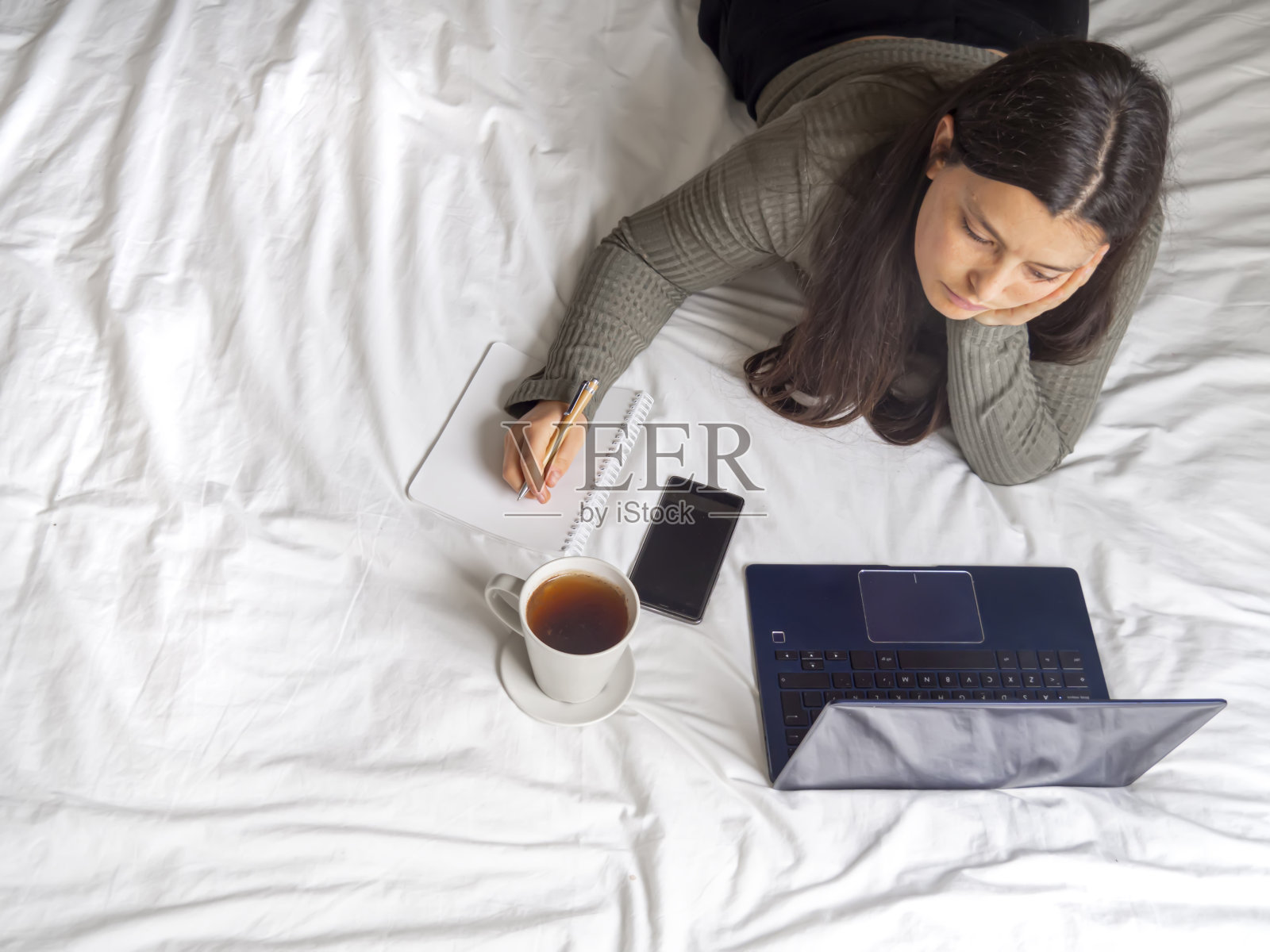 一个女人躺在床上无聊地看着笔记本电脑，在家里工作。照片摄影图片