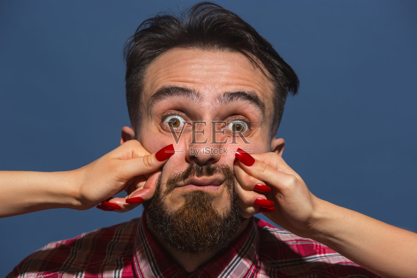 年轻男子的肖像与女性的手打他的脸在蓝色的背景照片摄影图片