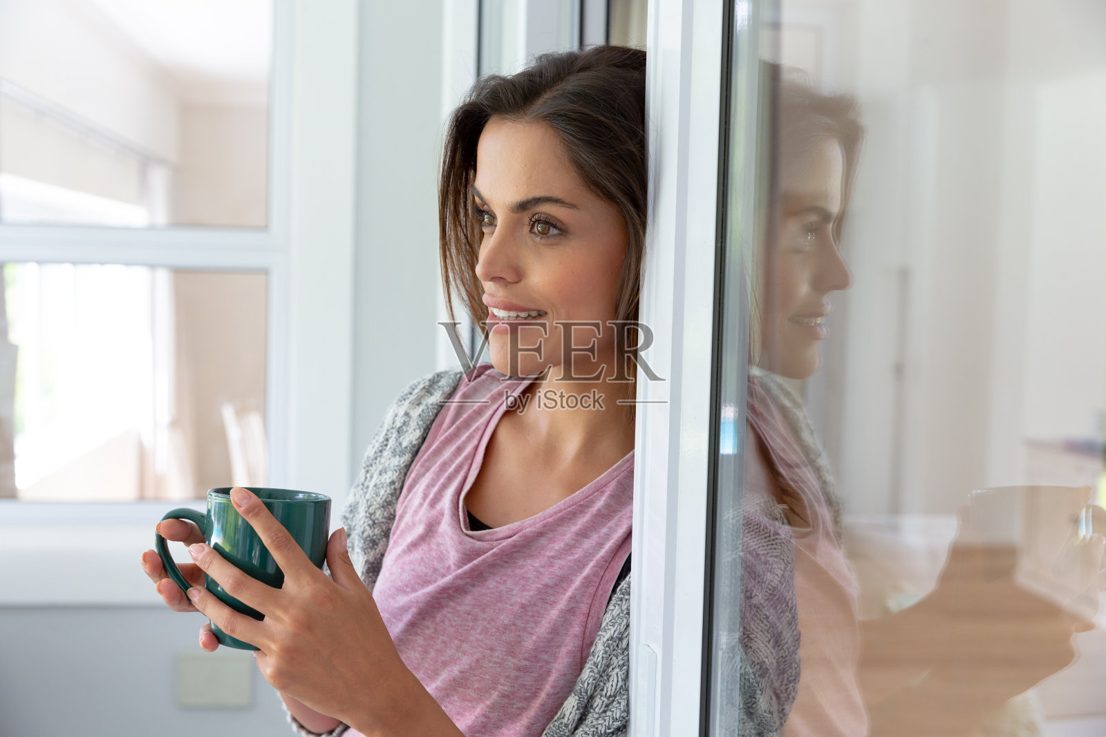 一个白人女人站在家里的窗边微笑着喝着咖啡照片摄影图片