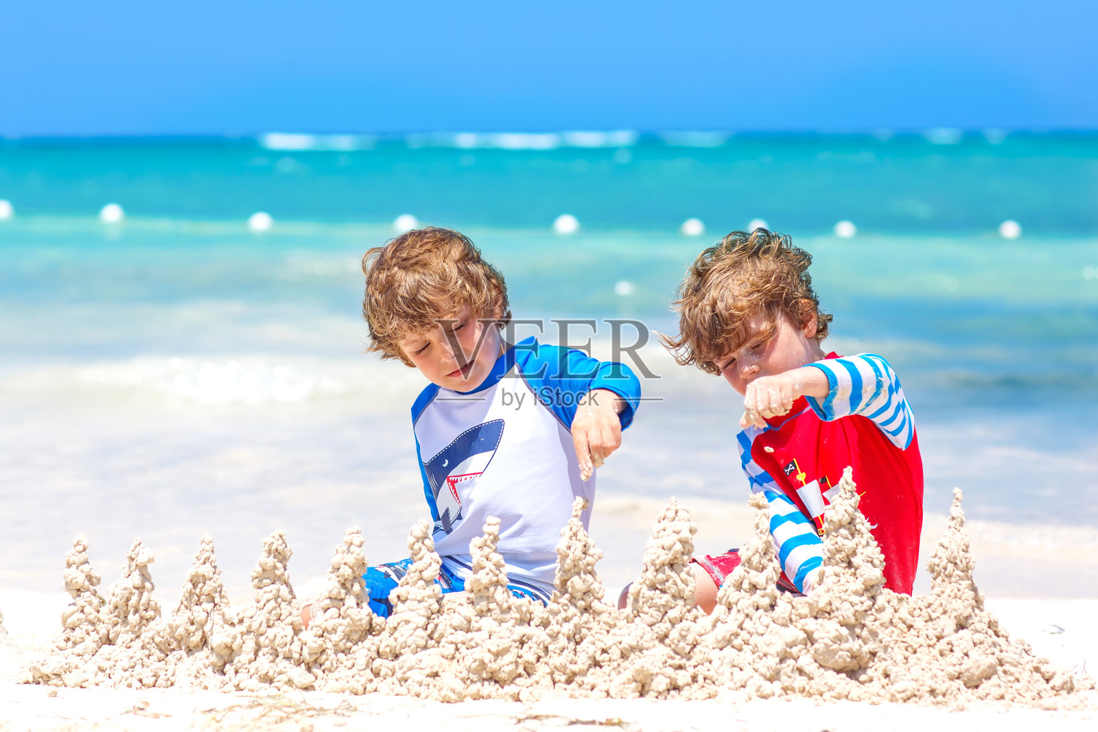 两个小男孩正在岛上的热带海滩上玩沙堡。健康的孩子们在一起度假。双胞胎，快乐的兄弟笑着笑着照片摄影图片