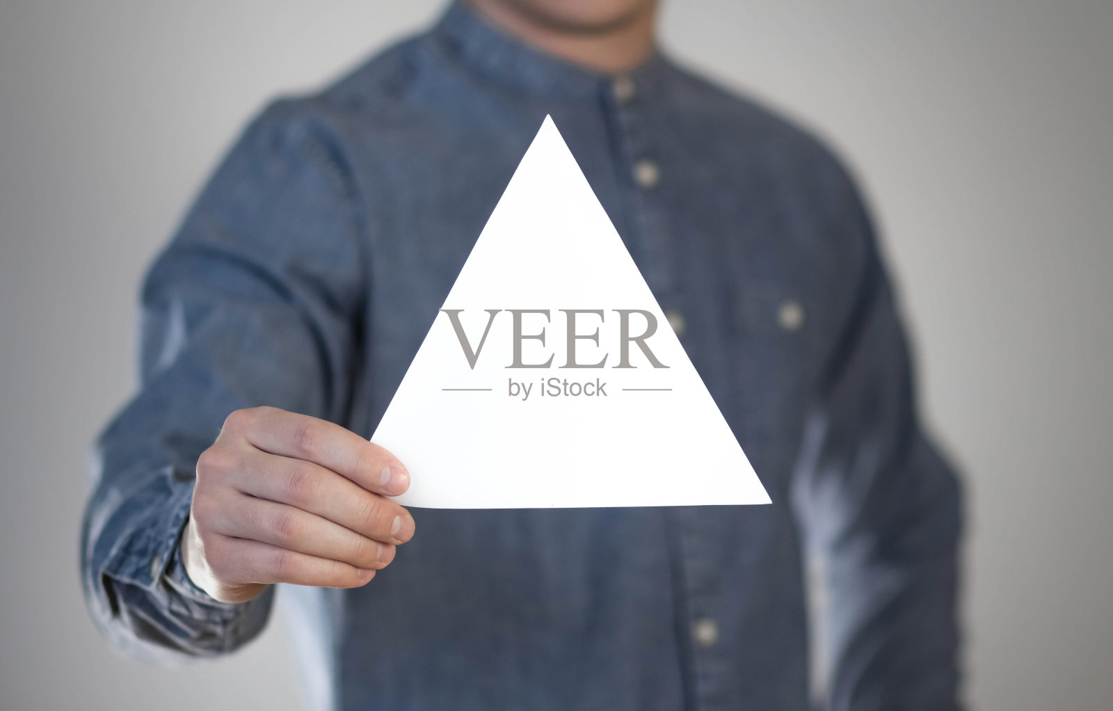 一个男人拿着一张白色的三角形的纸。一个人手里的传单。为你的文本做准备。孤立在灰色背景上照片摄影图片