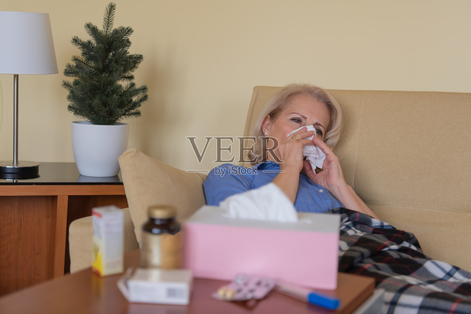 患流感的老年妇女躺在家里用纸巾打喷嚏。照片摄影图片