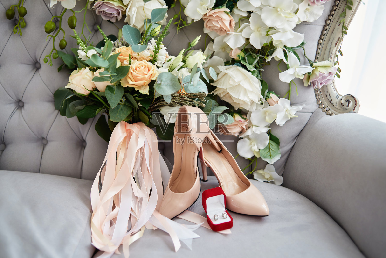 新娘花束玫瑰，小苍兰，布吕尼和桉树缎带，新娘鞋和耳环在薰衣草切斯特菲尔德椅子，复制空间。奢华的婚礼饰品和珠宝照片摄影图片