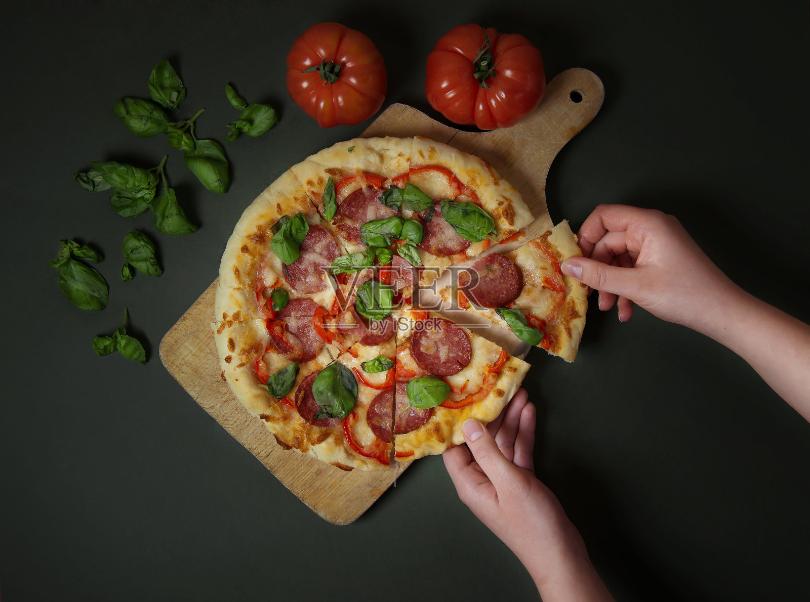 一个女人手里拿着一块披萨。意大利经典披萨，配以番茄和罗勒。深色背景上的意大利披萨。餐厅菜单和广告照片摄影图片