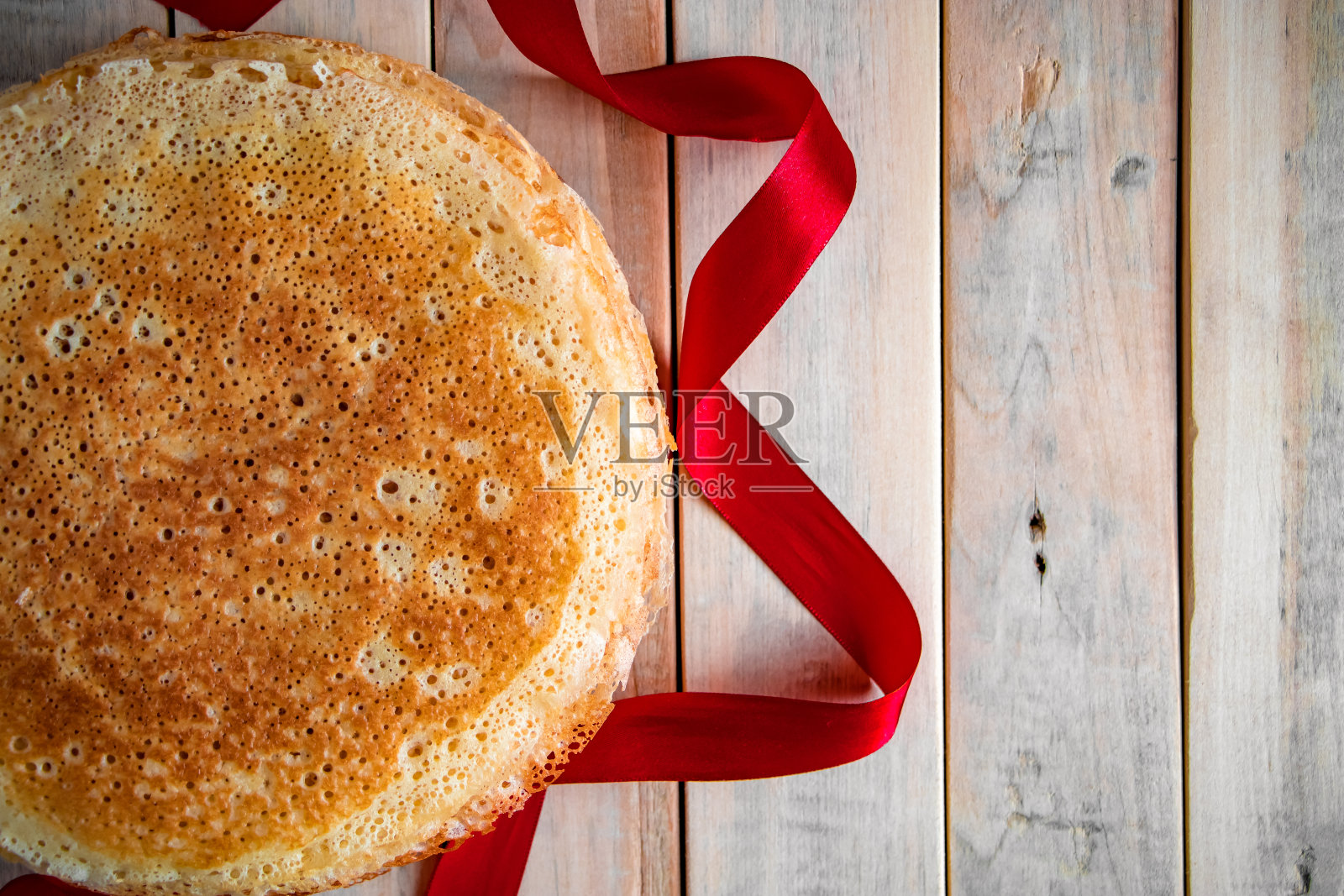 传统的俄罗斯薄煎饼特写在一个轻木制的背景和一个红色的缎带。照片摄影图片