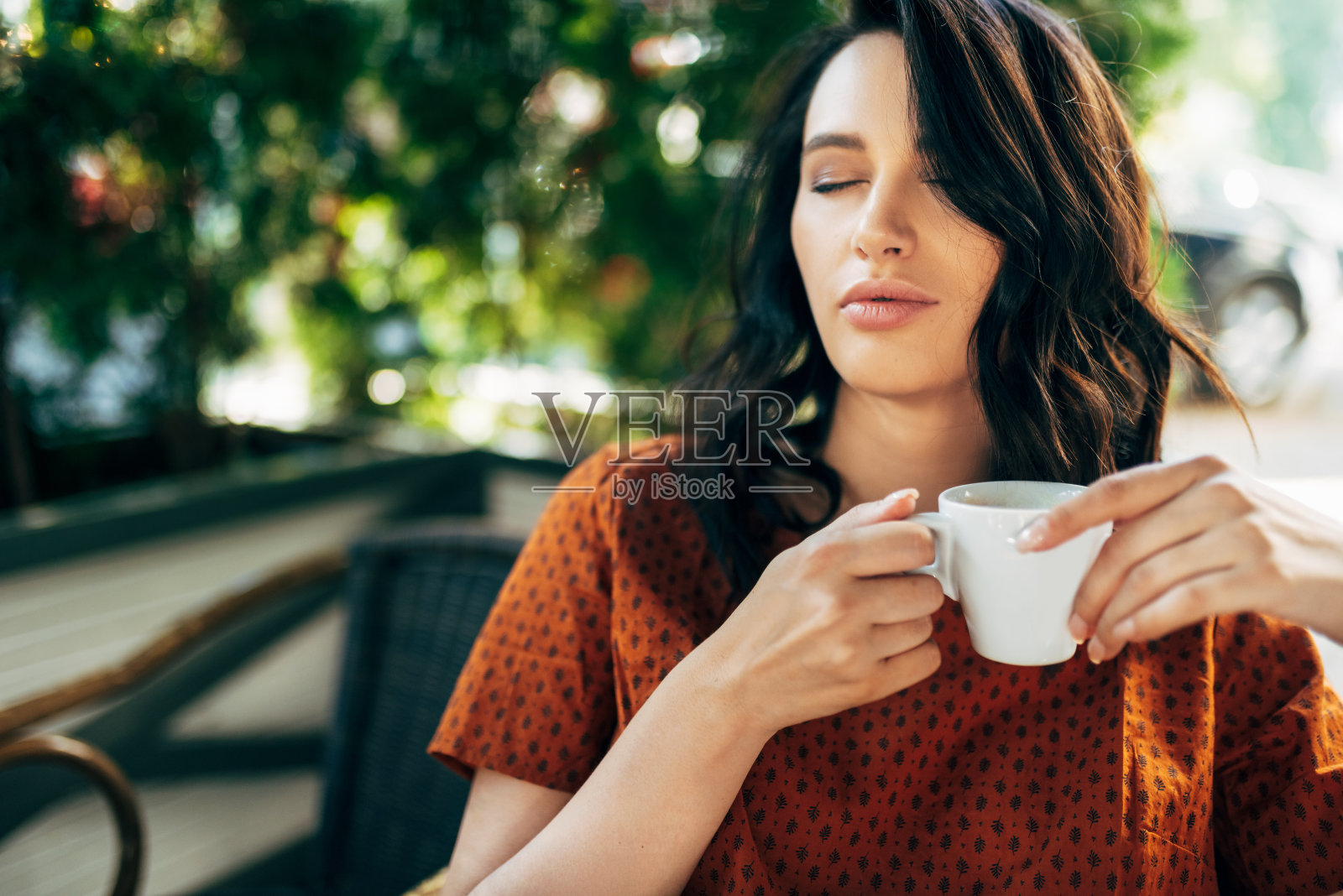 一个黑发女人在城市街道的自助餐厅喝咖啡在早上的偷拍肖像。照片摄影图片