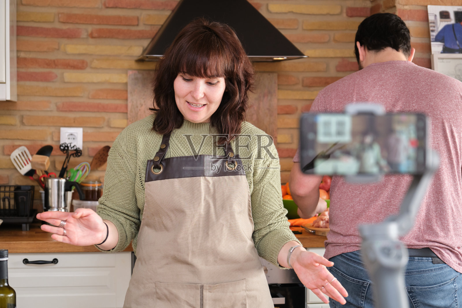 一名年轻女子一边解释食谱，一边用智能手机为她的烹饪频道录制视频。内容创造者和影响者。照片摄影图片