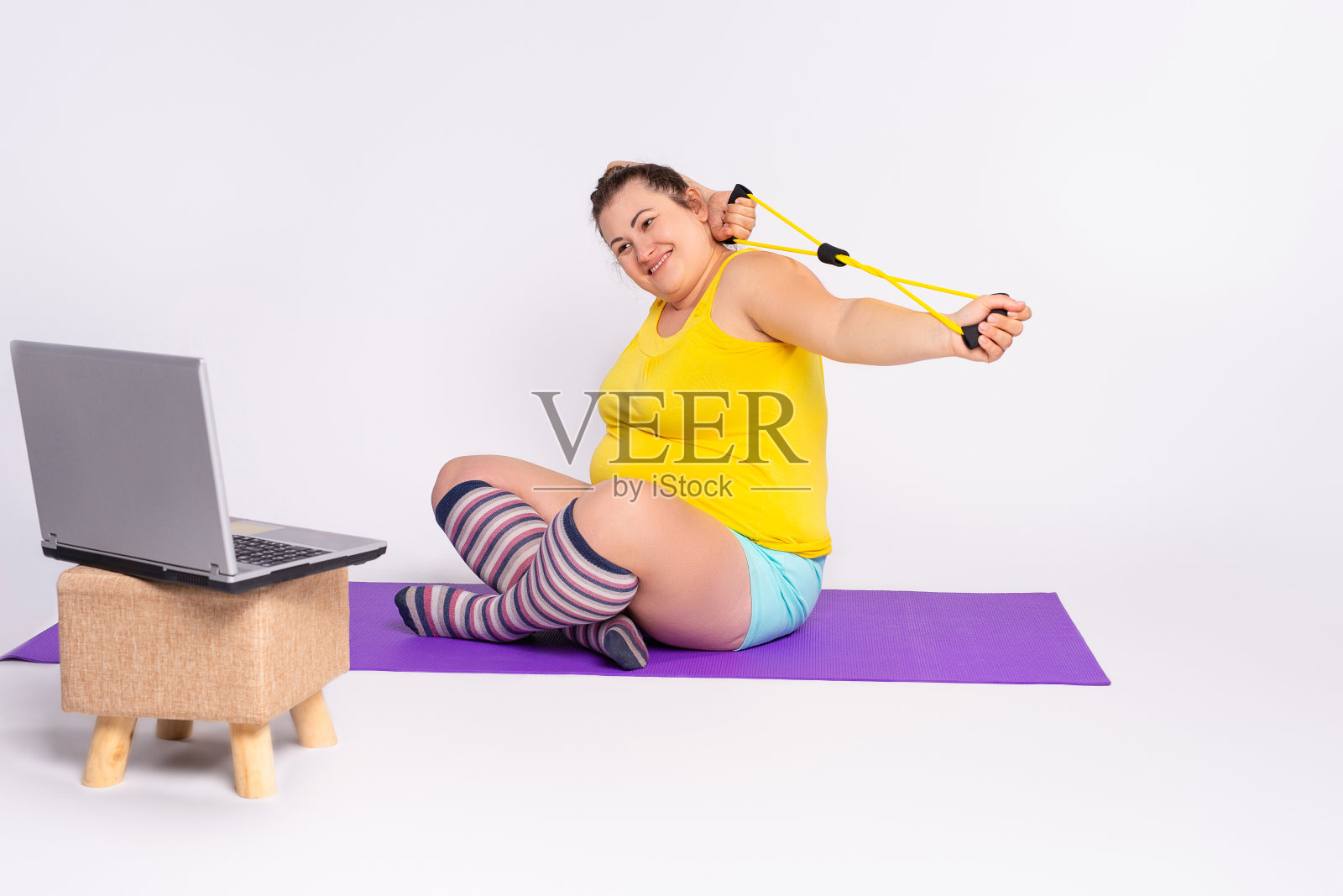 胖女人在家在笔记本电脑前锻炼。加大尺寸，网上运动运动用阻带，女性用曲线的身体训练来减肥，得到强壮柔韧的身体照片摄影图片