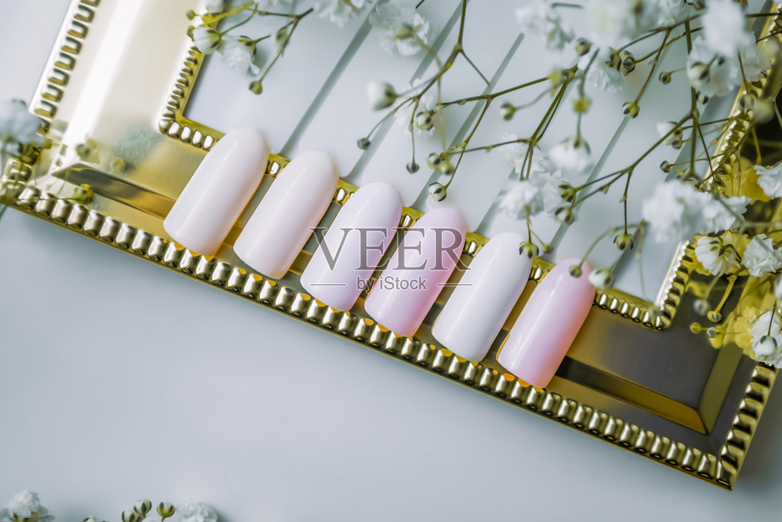 夏日指甲油的样品。指甲测试仪在一个白色的背景和一个金色的框架与gypsophila花。照片摄影图片