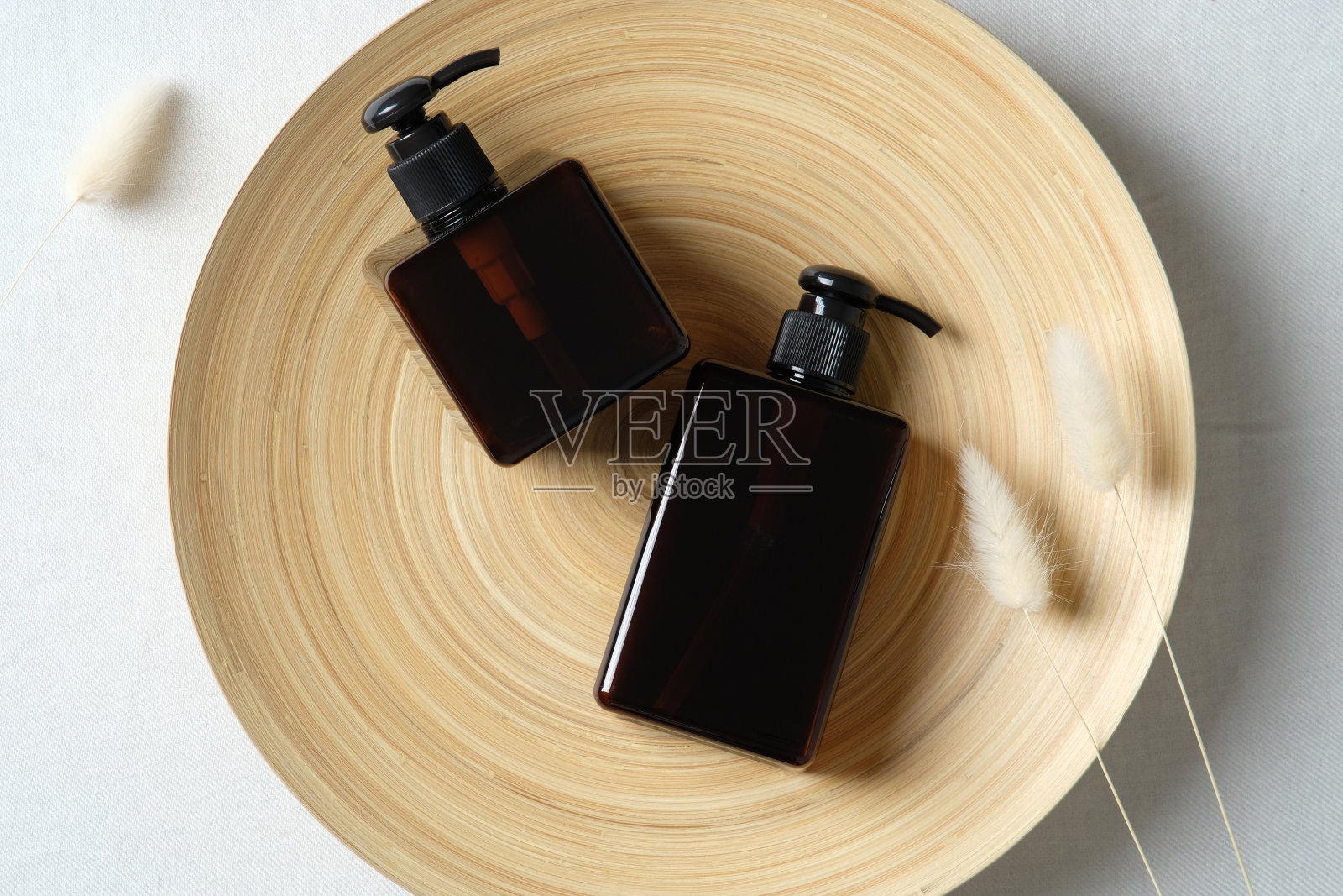 天然护肤SPA化妆品瓶子和干花在盘子上。深琥珀色的玻璃容器装洗发水或液体肥皂。平的。前视图。照片摄影图片