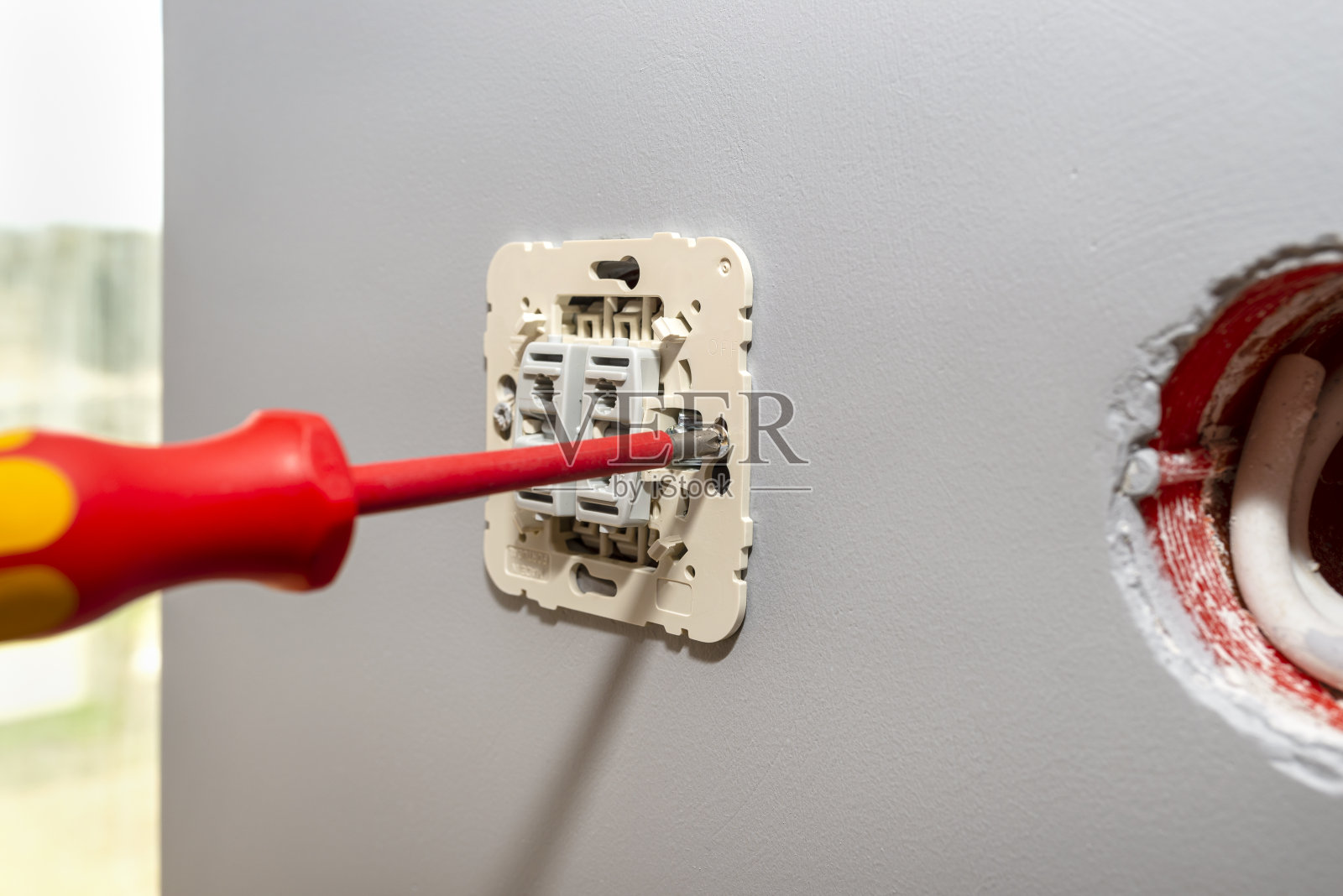 在窗边的房间里，用一把红色螺丝刀上下转动卷帘门的开关。照片摄影图片